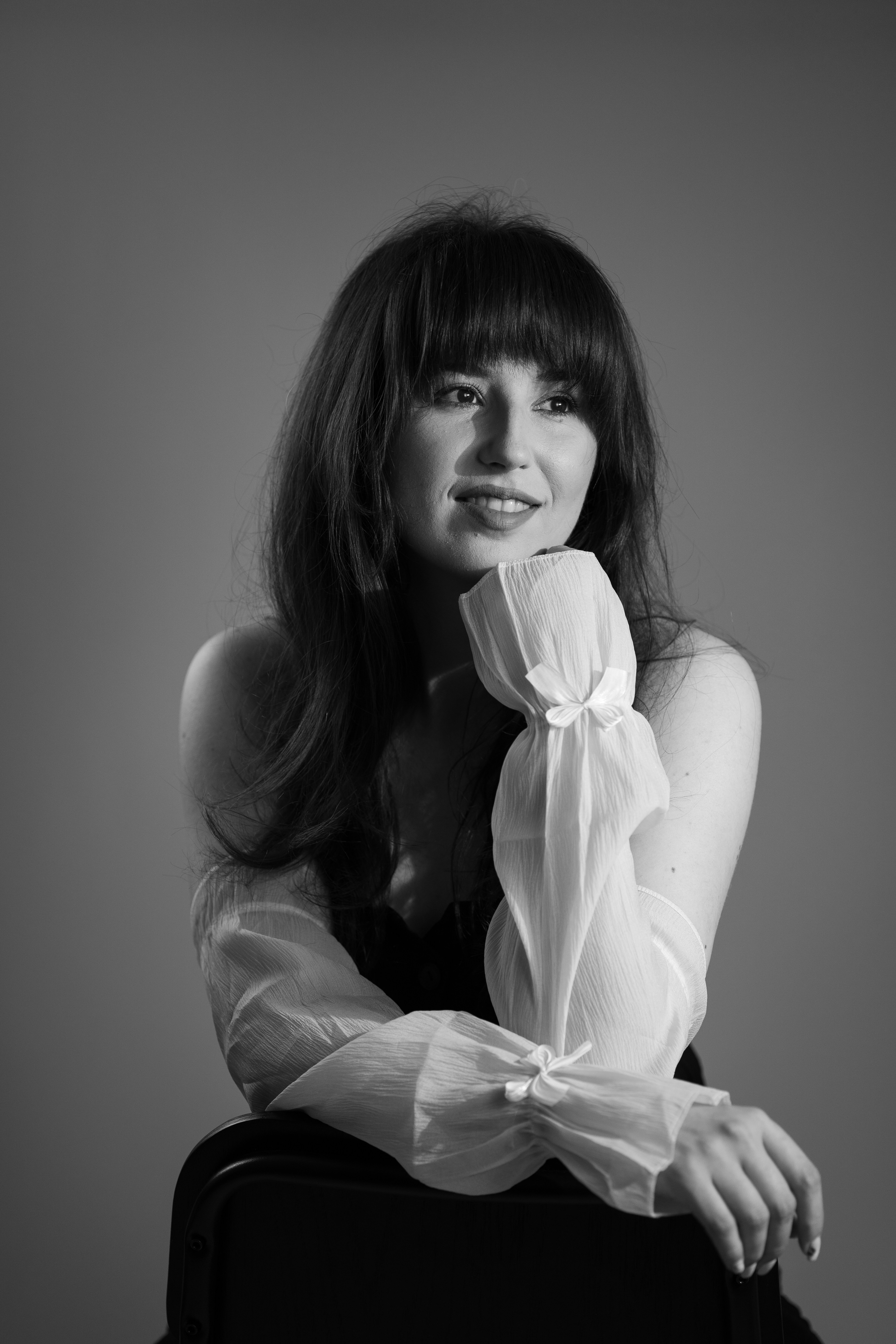 Joven con flequillo sonríe, apoyando la barbilla en la mano.