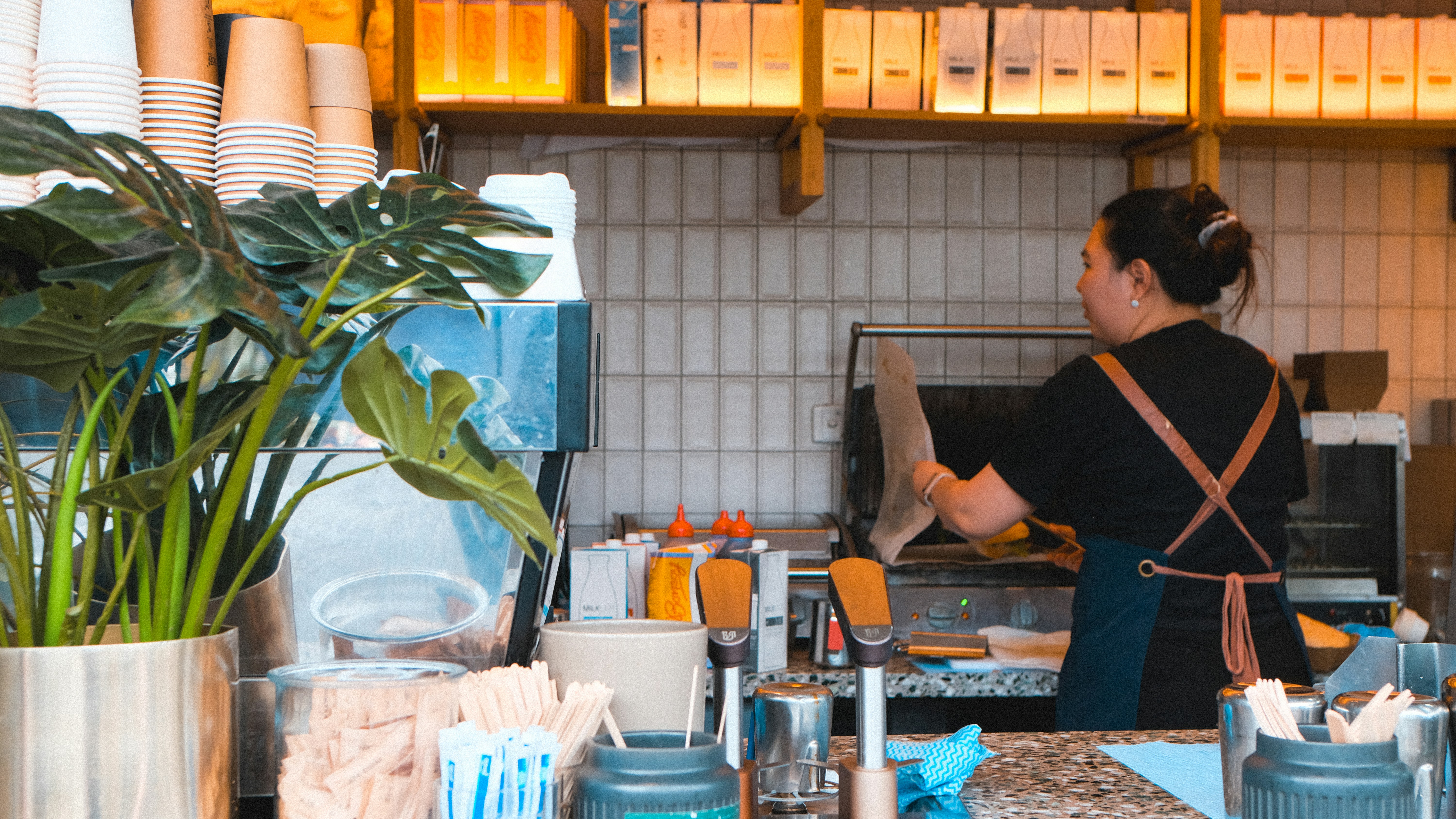 Barista preparando bebidas atrás de um balcão com plantas.