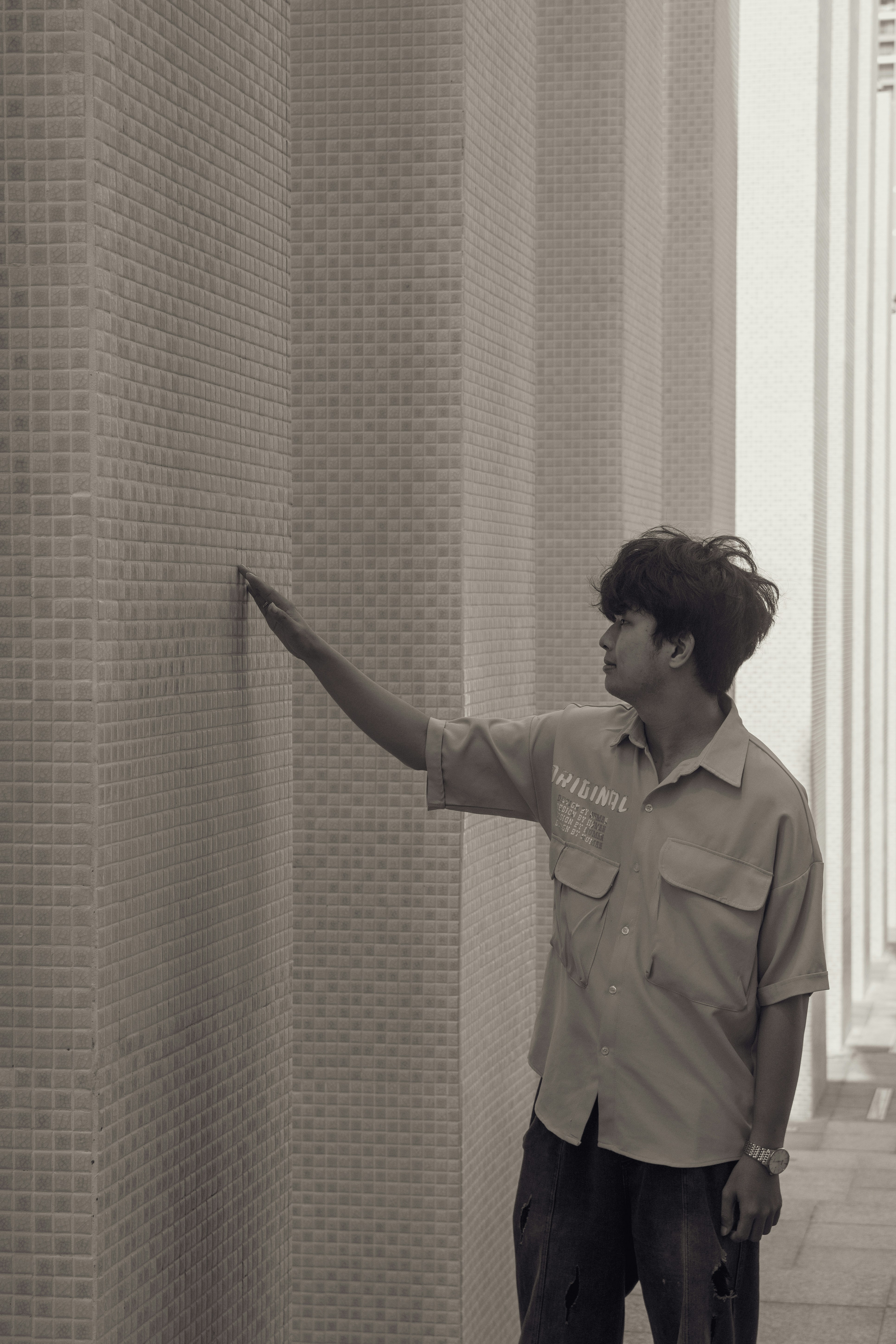 A man touches a tiled wall with his hand.