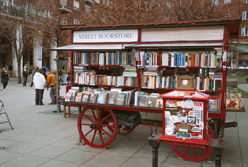 A red street bookstore cart filled with books.