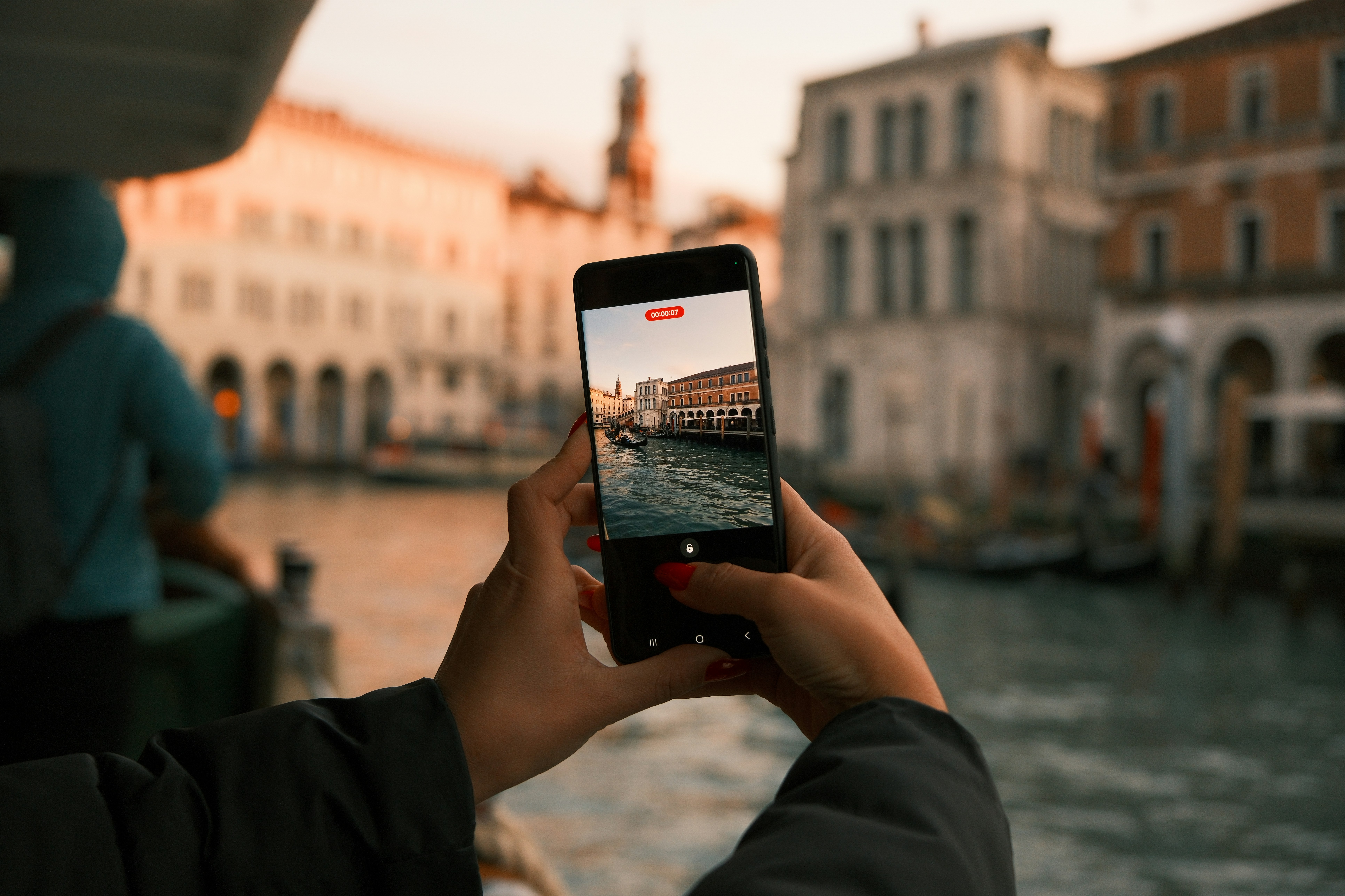Hands holding smartphone recording canal buildings at sunset