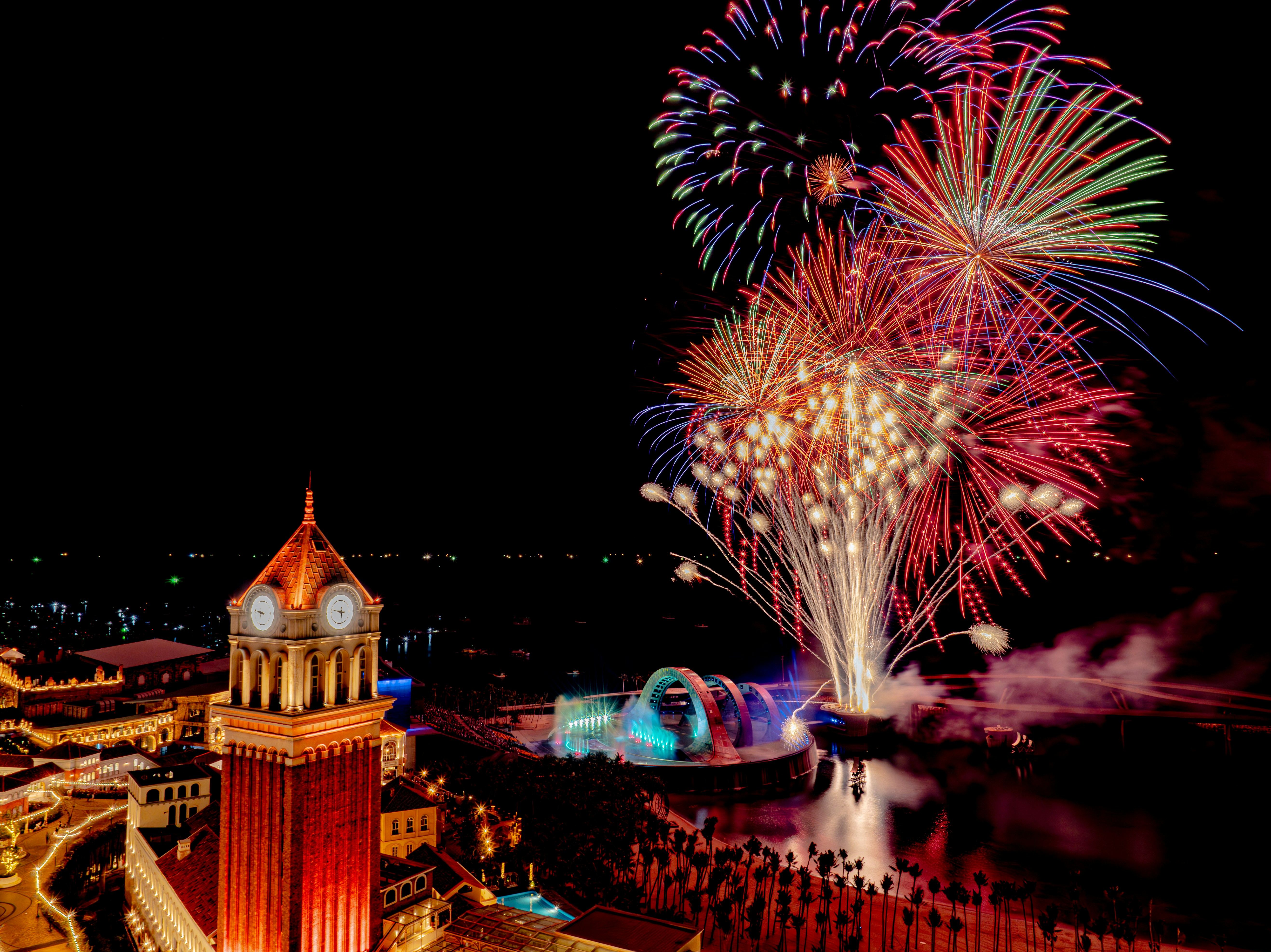 Colorful fireworks explode over a cityscape at night.