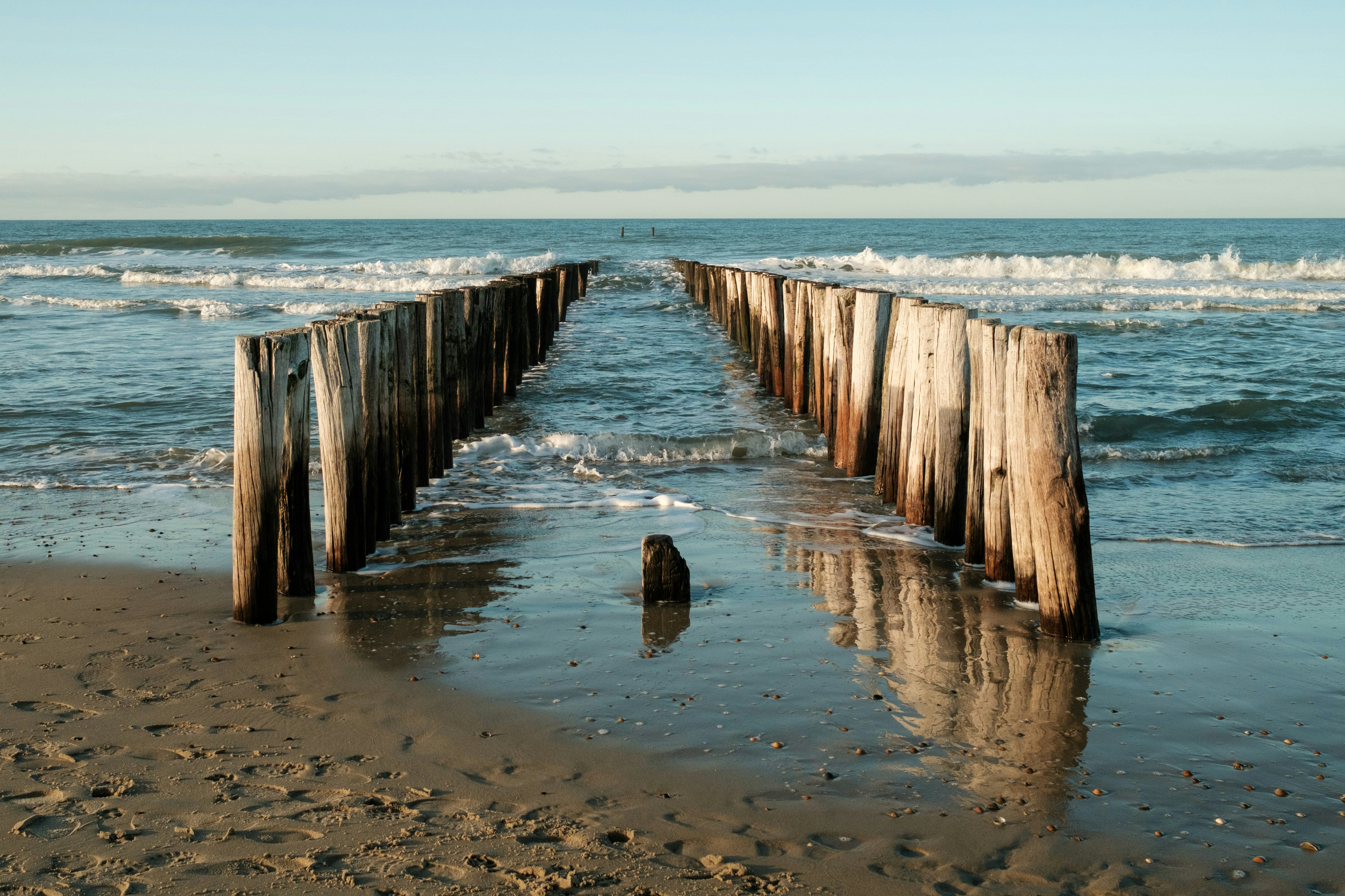 Weathered wooden posts line a beach leading to the ocean
