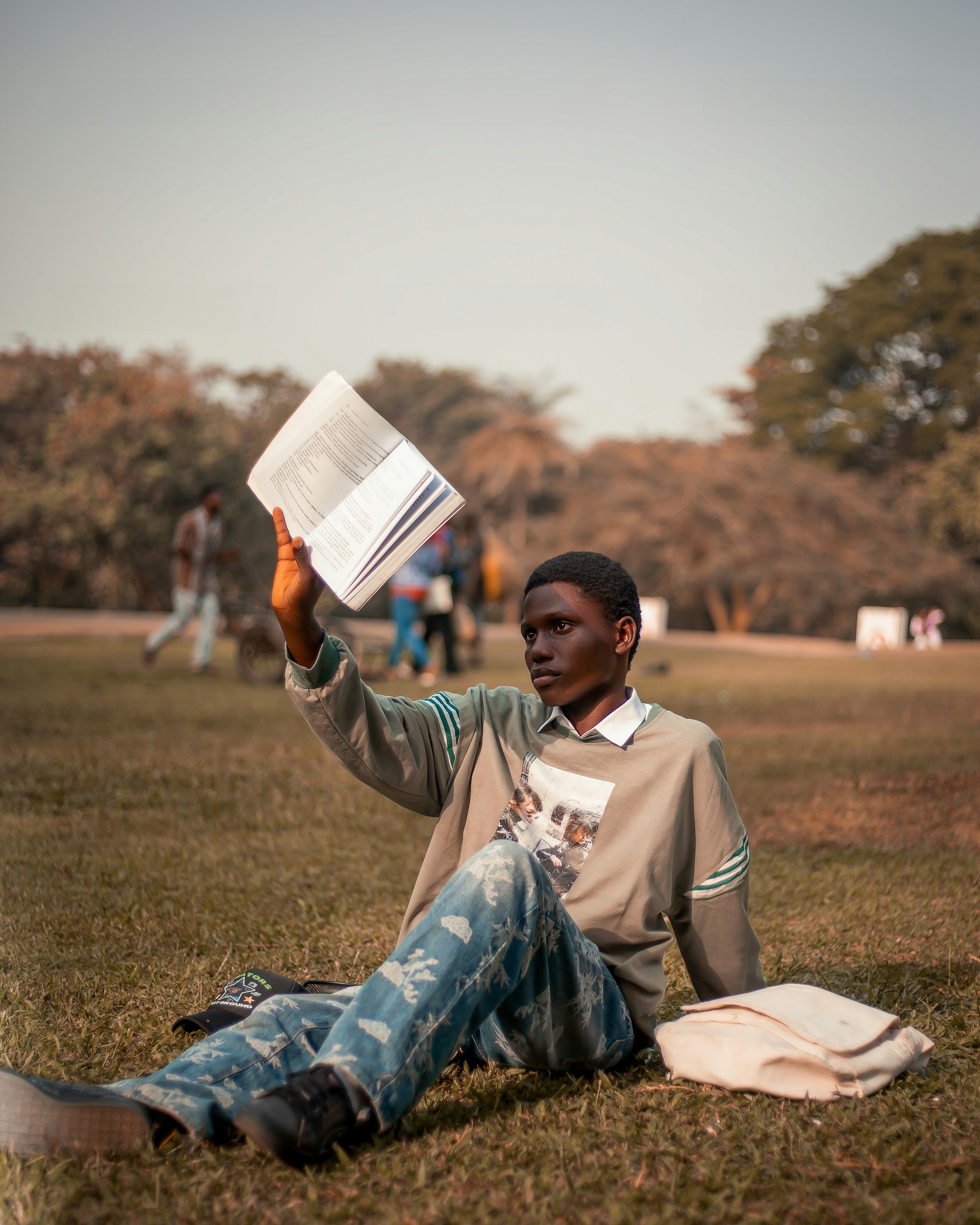 Young man sitting on grass reading a book outdoors