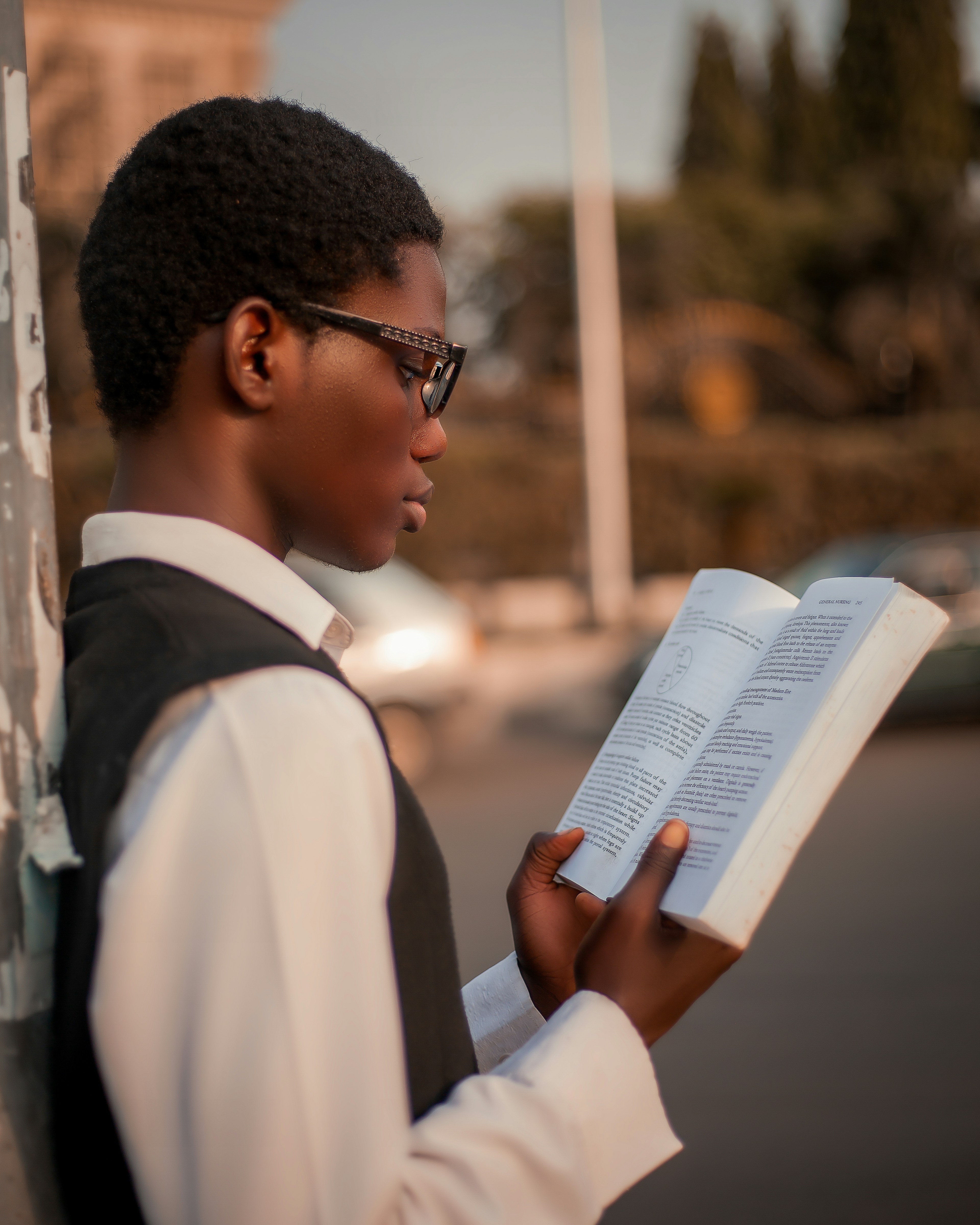 Un giovane con gli occhiali legge un libro all'aperto.