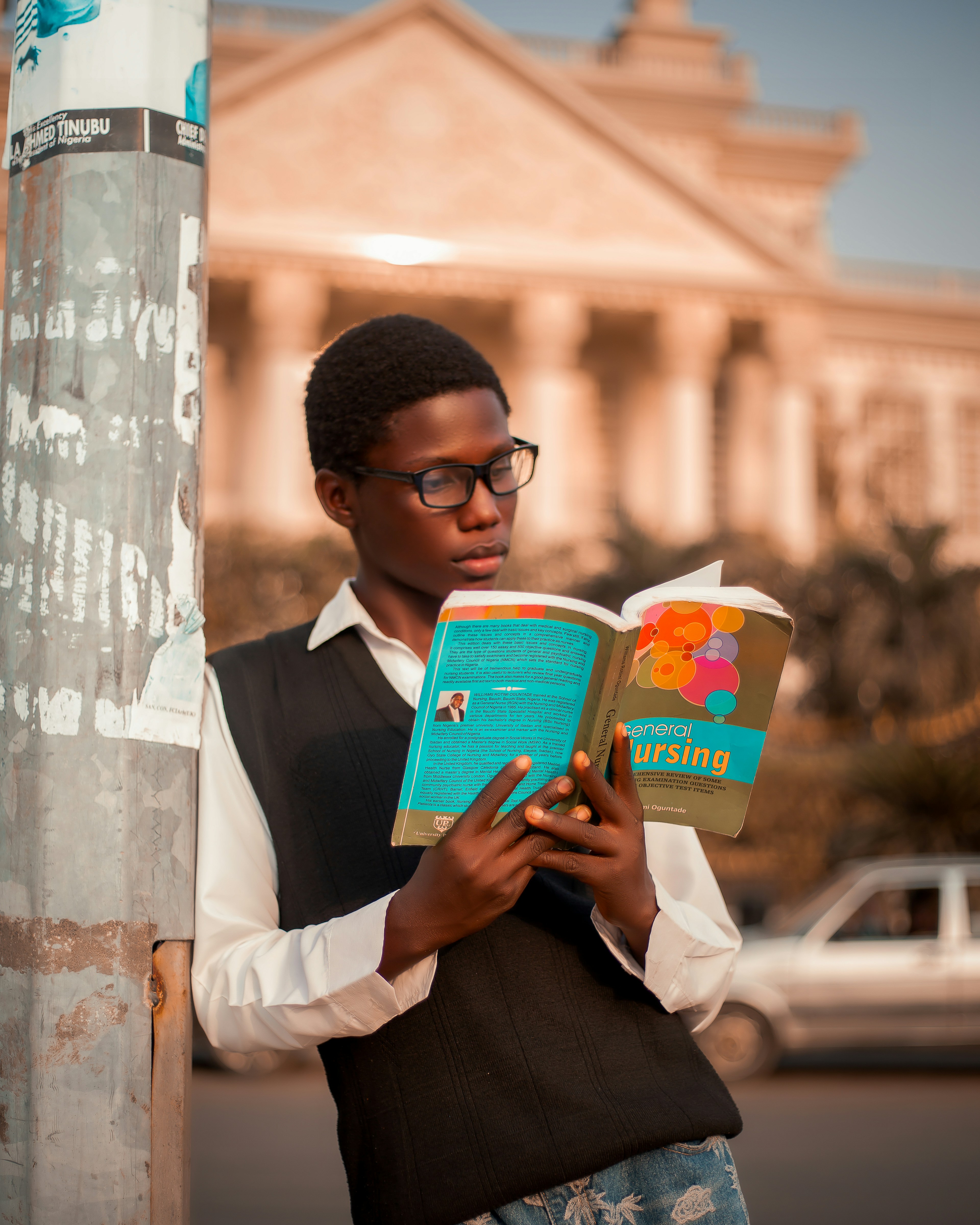 Young man wearing glasses reading a textbook outdoors.