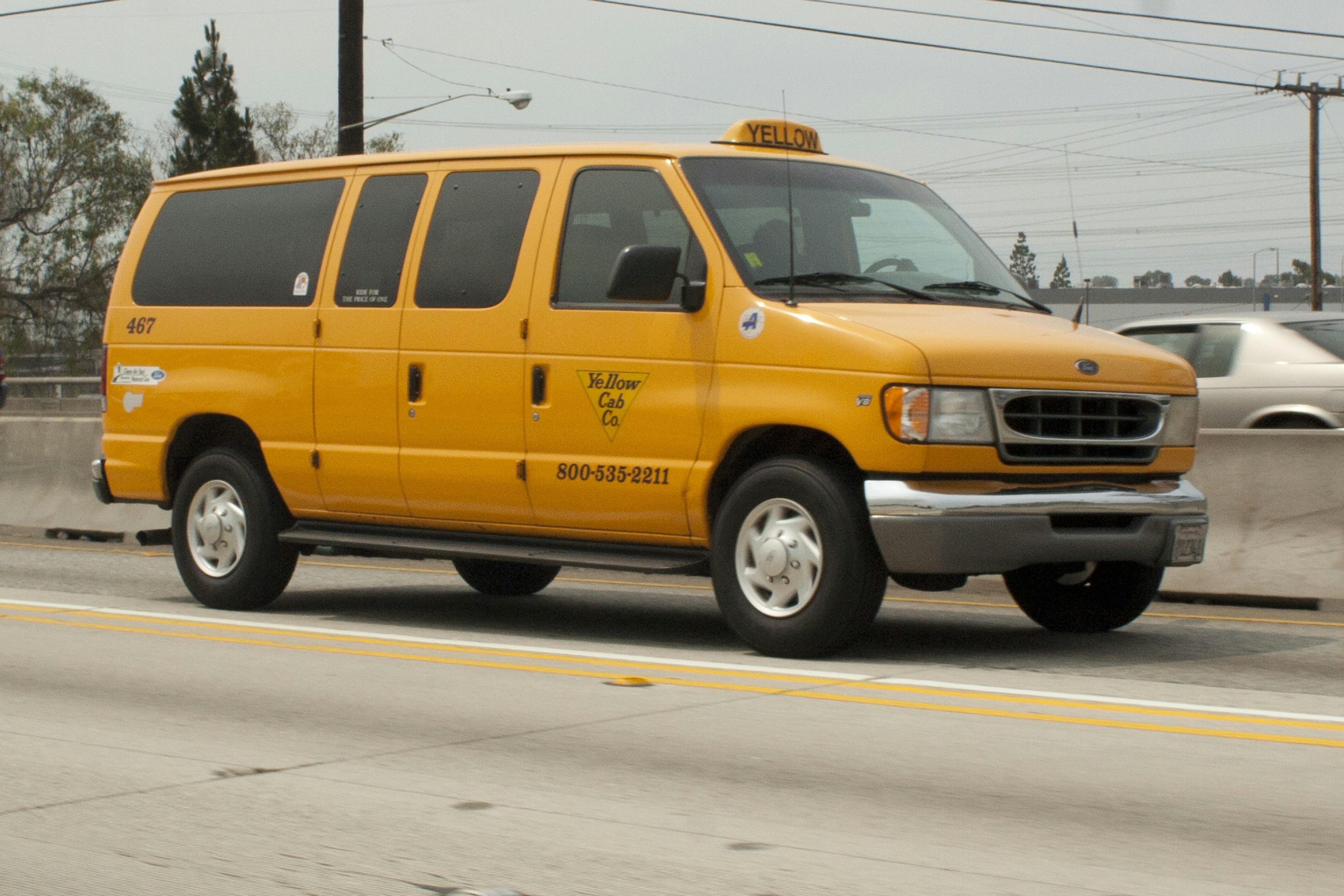 A yellow taxi van driving on a highway.