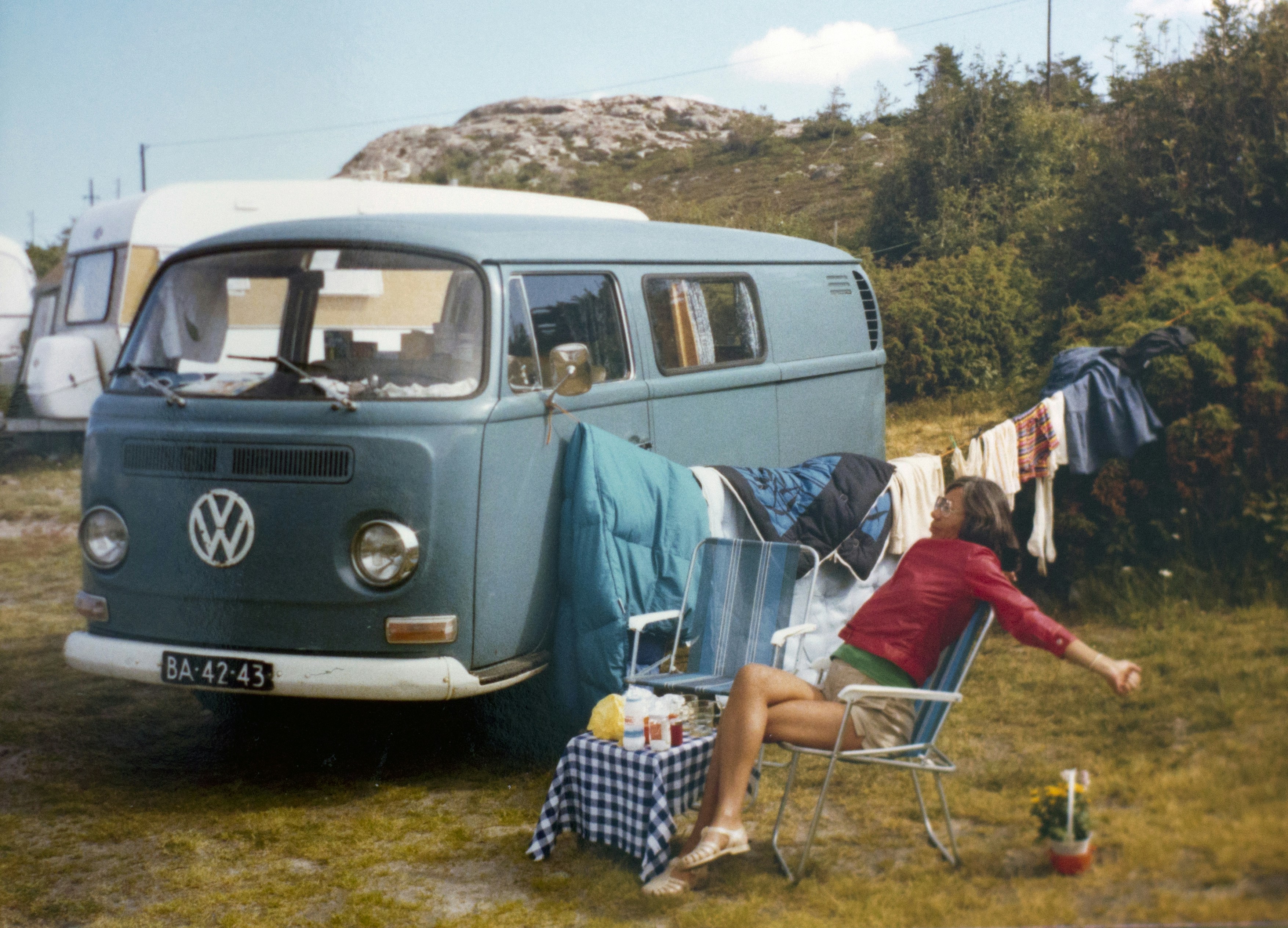 Woman relaxing by blue camper van at campsite