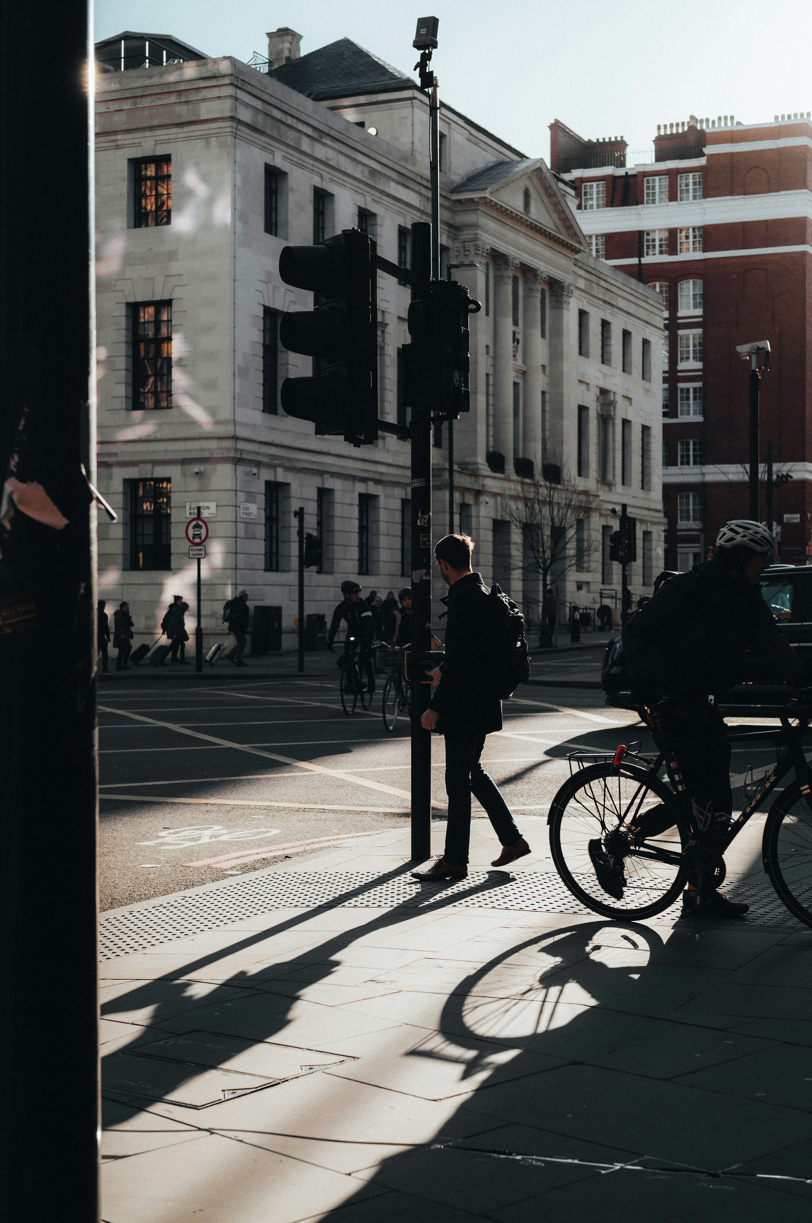 Pedestrians and cyclist at a city intersection with long shadows.