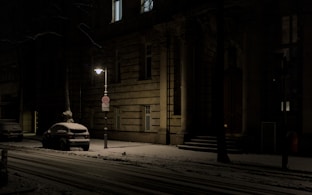 Snowy street with a parked car at night.