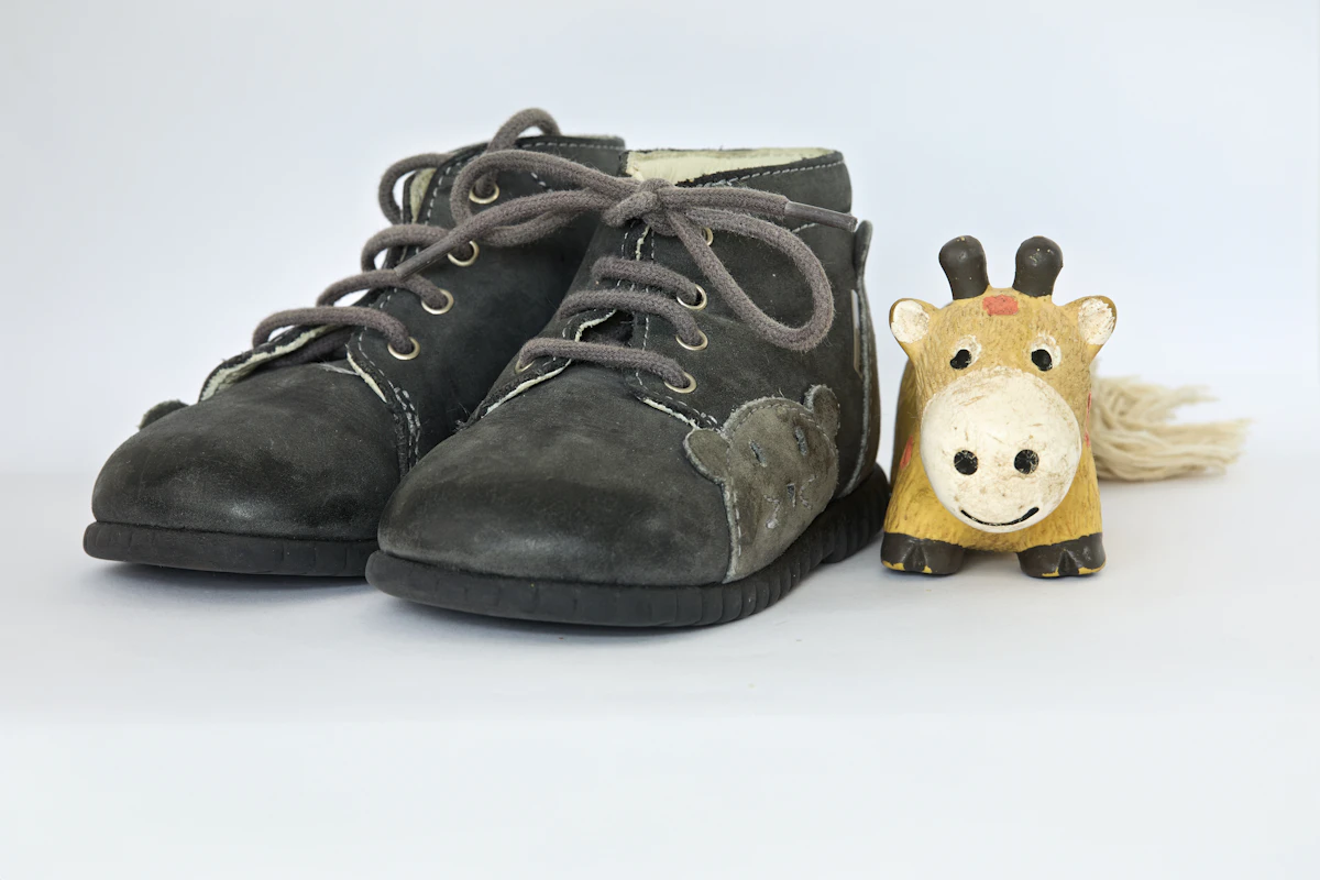 Sepasang sepatu bayi abu-abu di samping mainan jerapah kayu