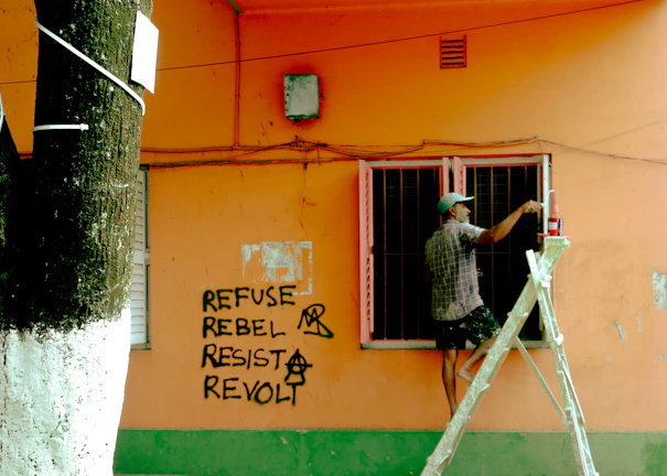 Man on ladder paints wall with graffiti