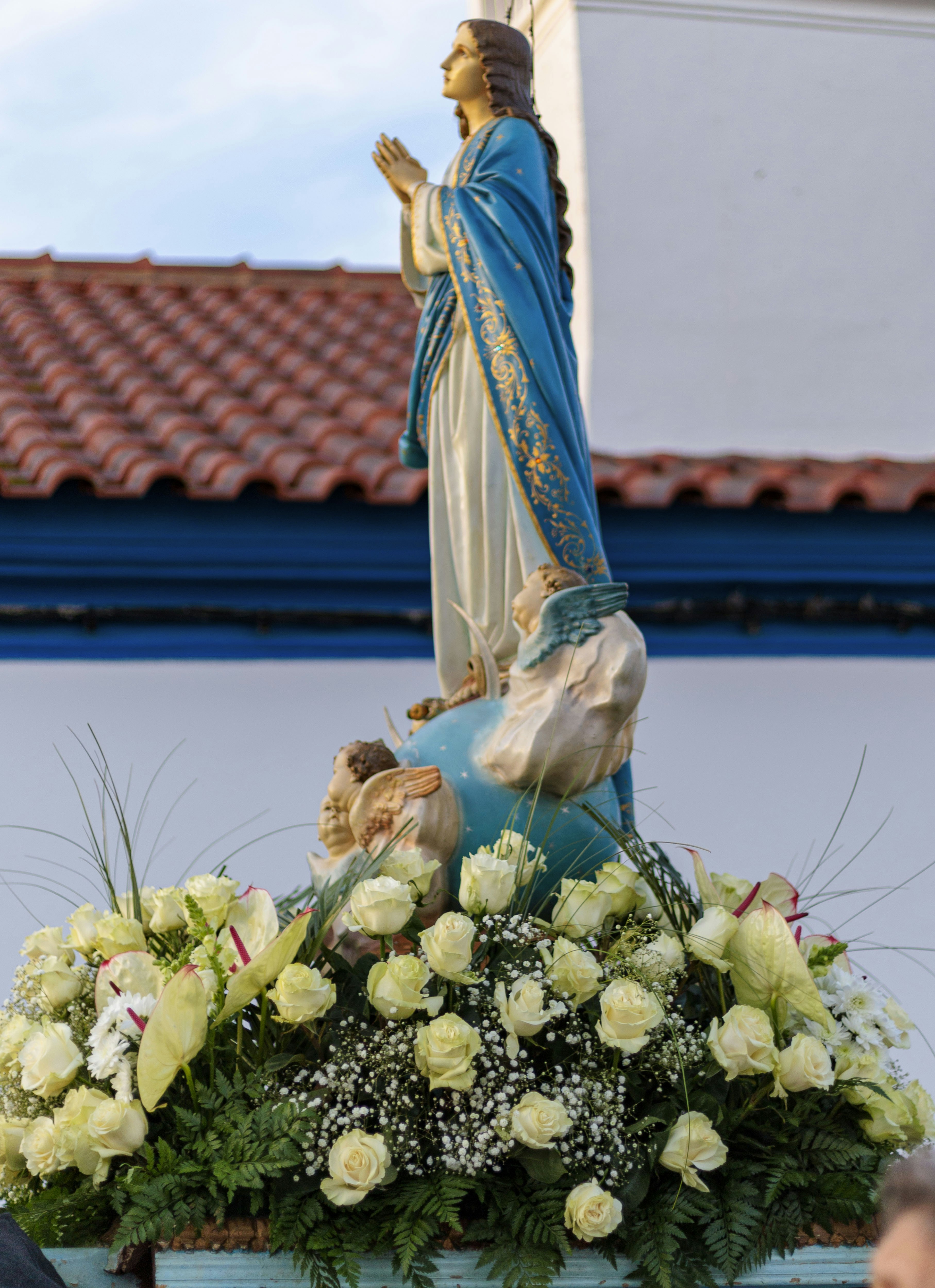 Statue of mary adorned with white roses and greenery