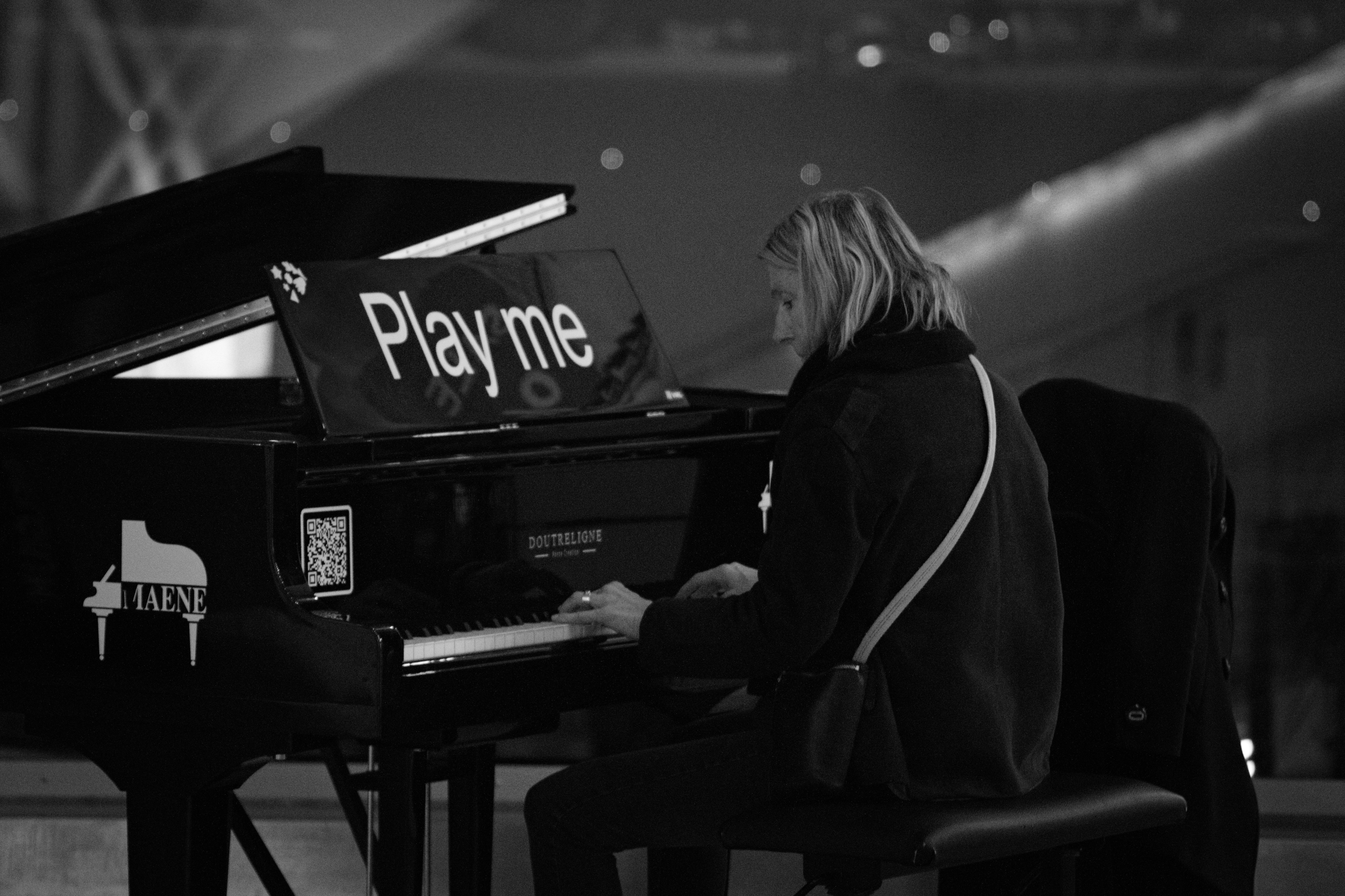 Woman playing a grand piano with "play me" sign.