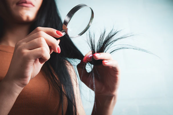 Woman examining split ends of hair with magnifying glass
