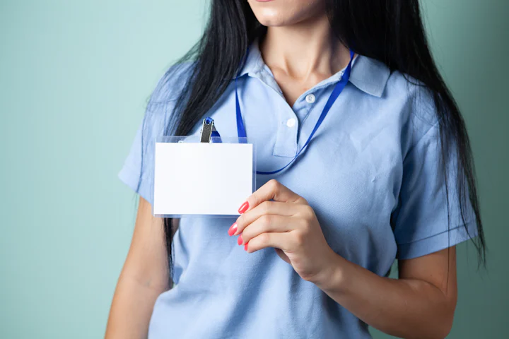 A person in a blue shirt holding a blank name badge on a lanyard.