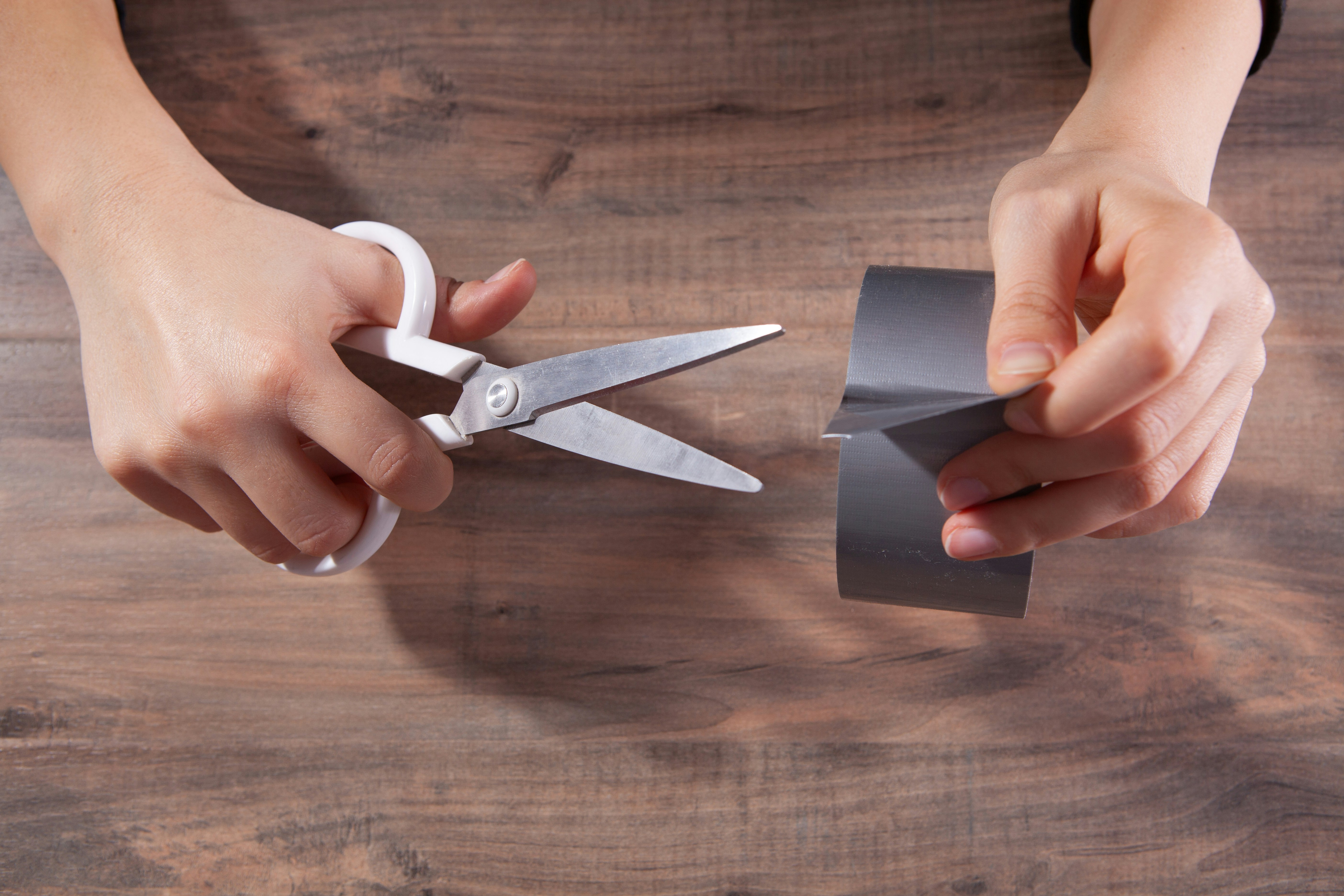 Hands cutting grey duct tape with scissors