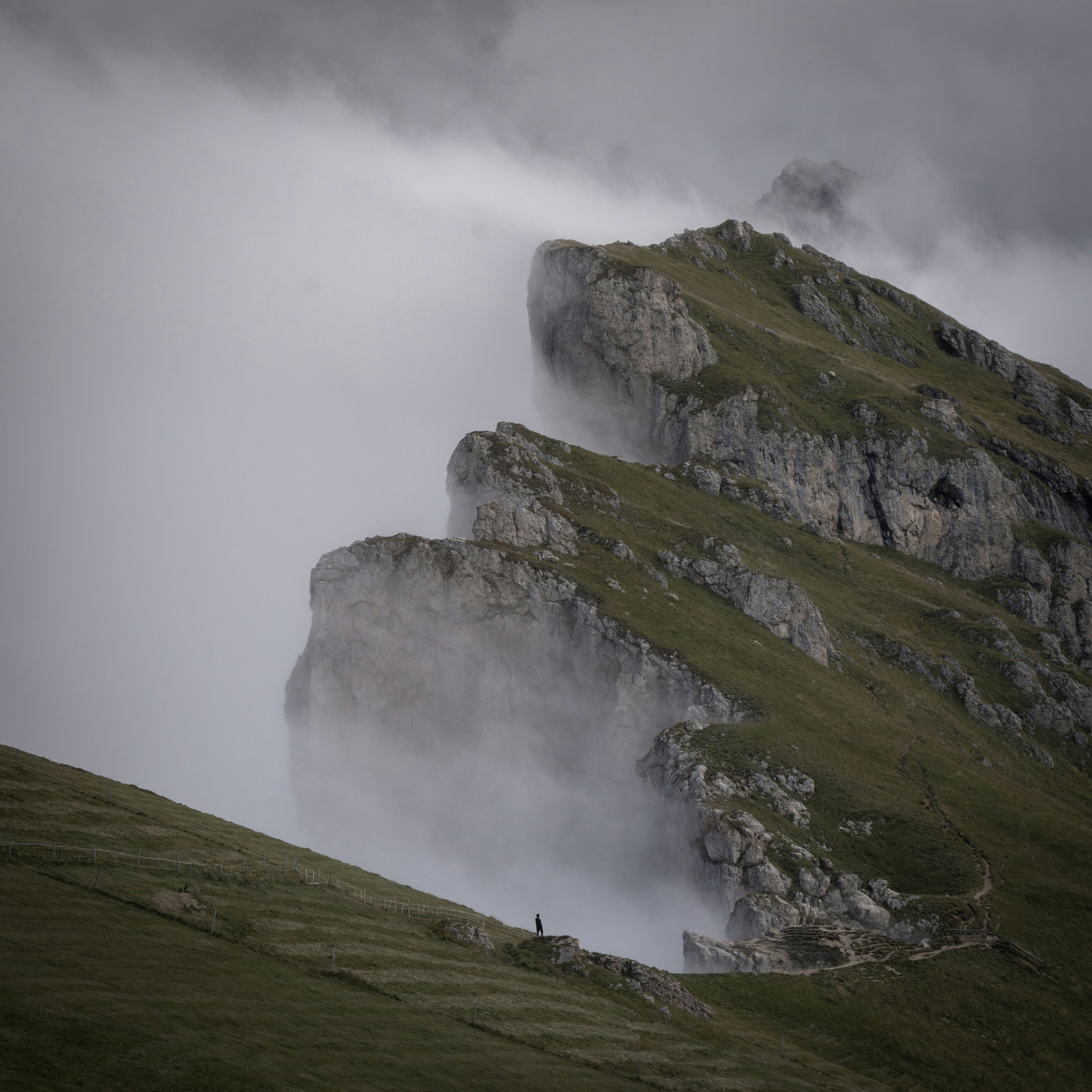 Un escursionista solitario su una cresta erbosa di montagna nella nebbia