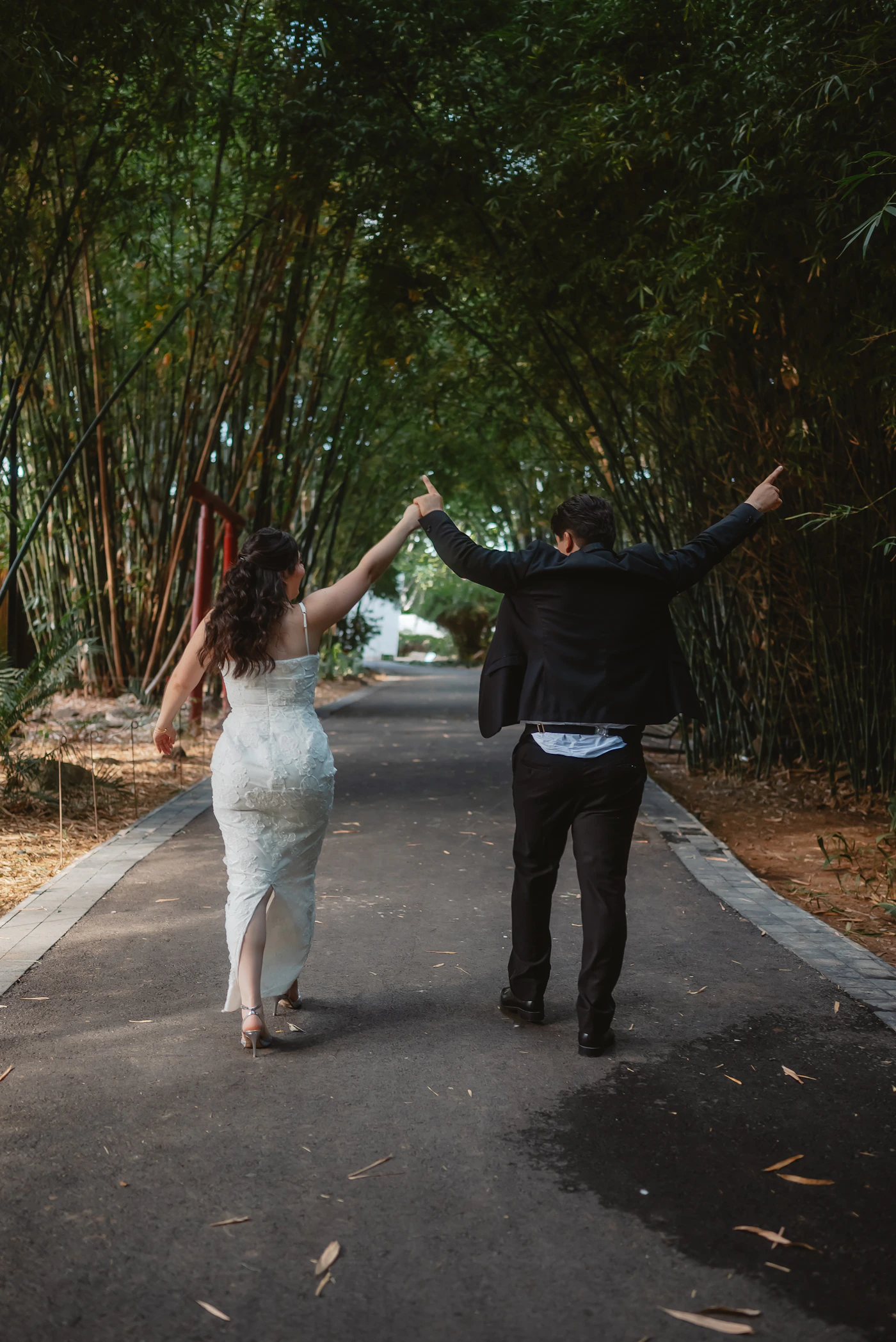Couple walking together down a lush bamboo-lined green path in wedding attire, natural soft filtered light