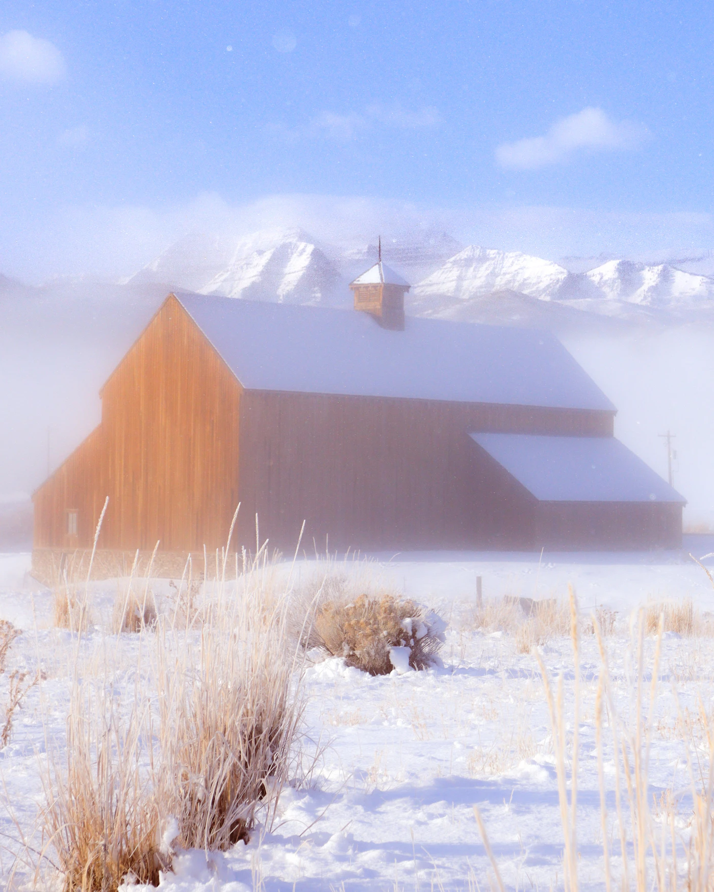 A wooden barn in a snowy, foggy mountain valley