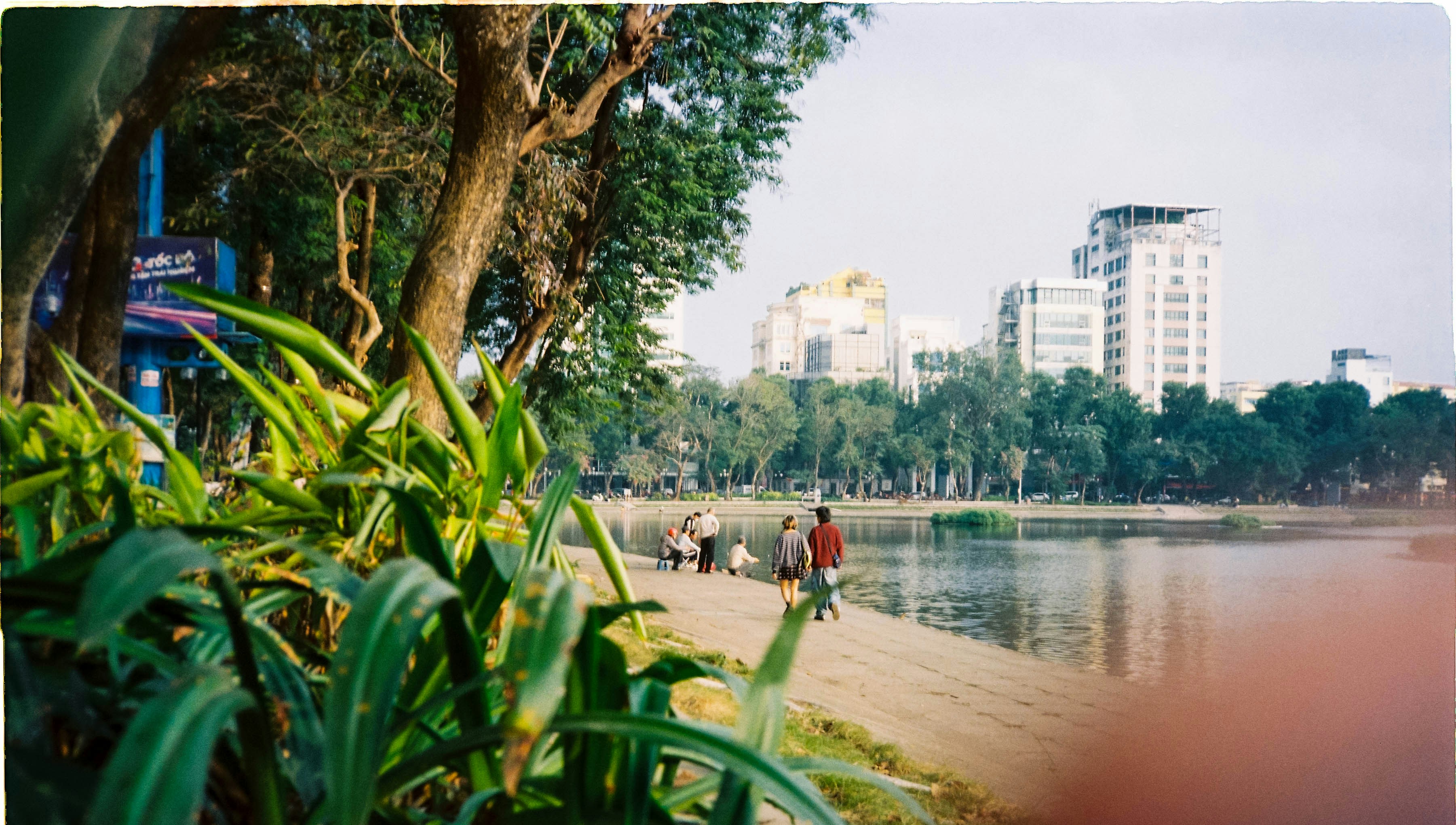 People walking by a lake with city buildings in background