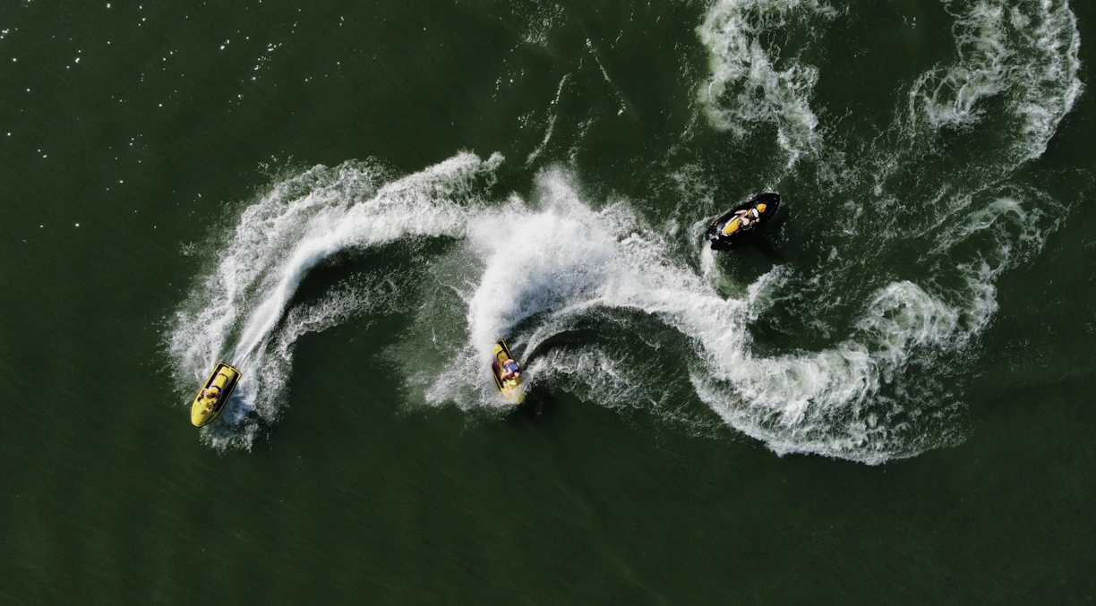 Three jet skiers creating white wakes on green water