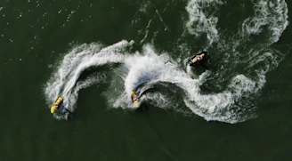 Three jet skiers creating white wakes on green water