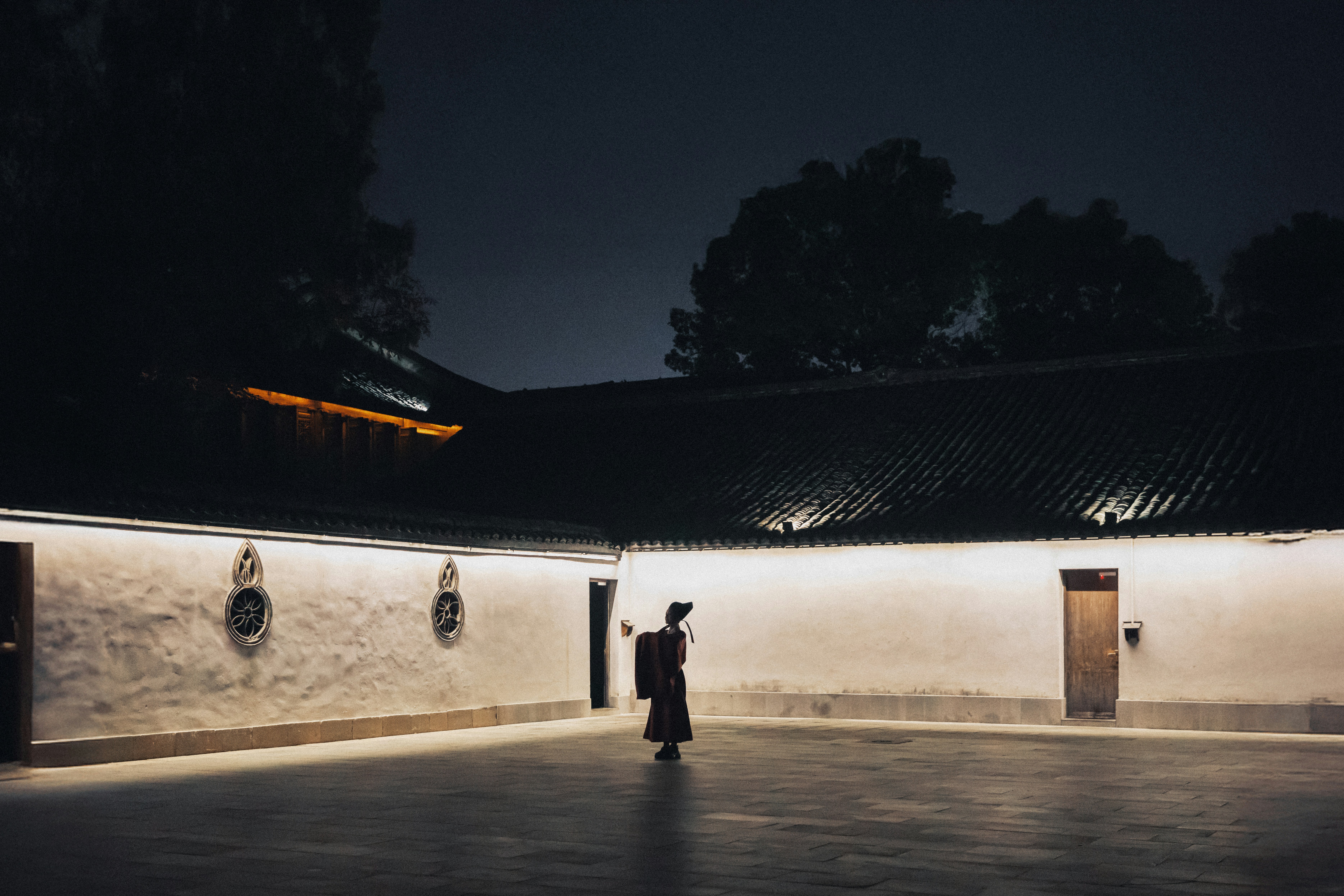 Figure in traditional clothing stands in courtyard at night