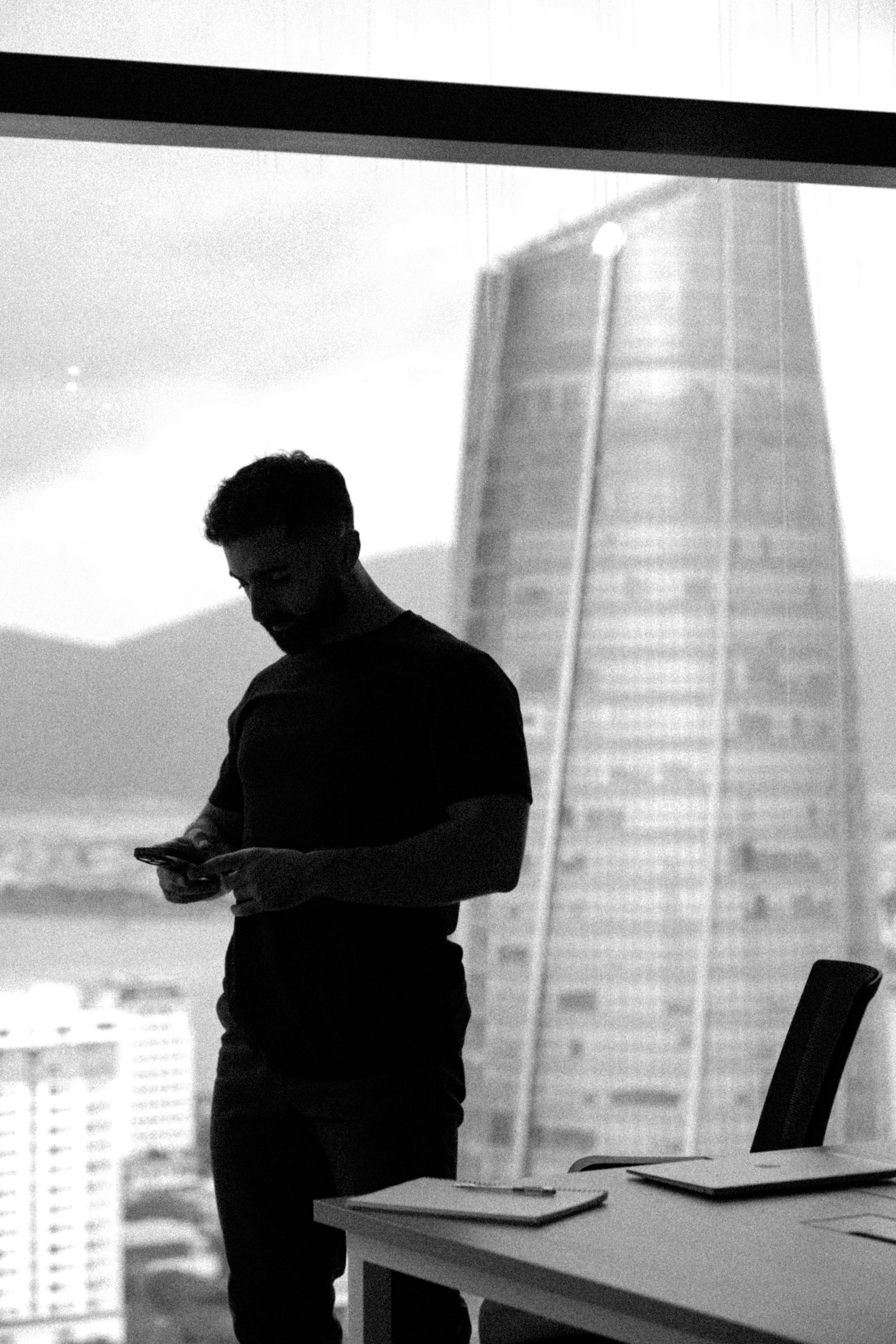 Man looking at phone by office window with city view