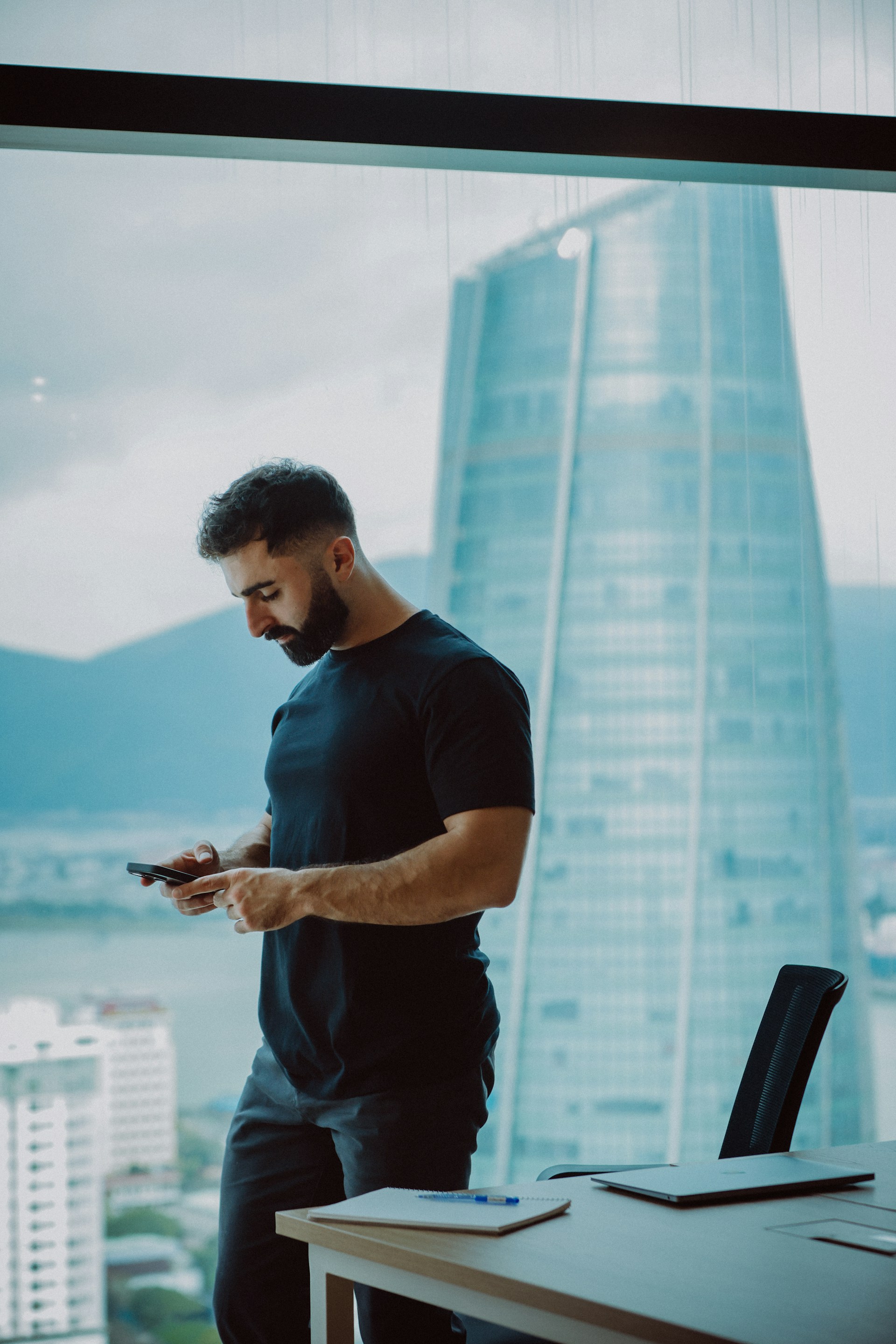 Man in black shirt texting on phone by office window