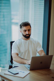 Man working on laptop at desk with city view.