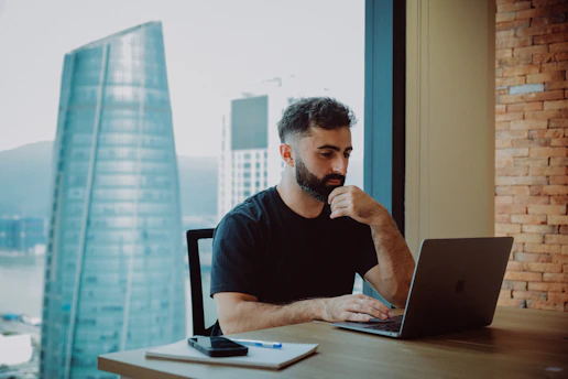 Man working on a laptop by a large window.