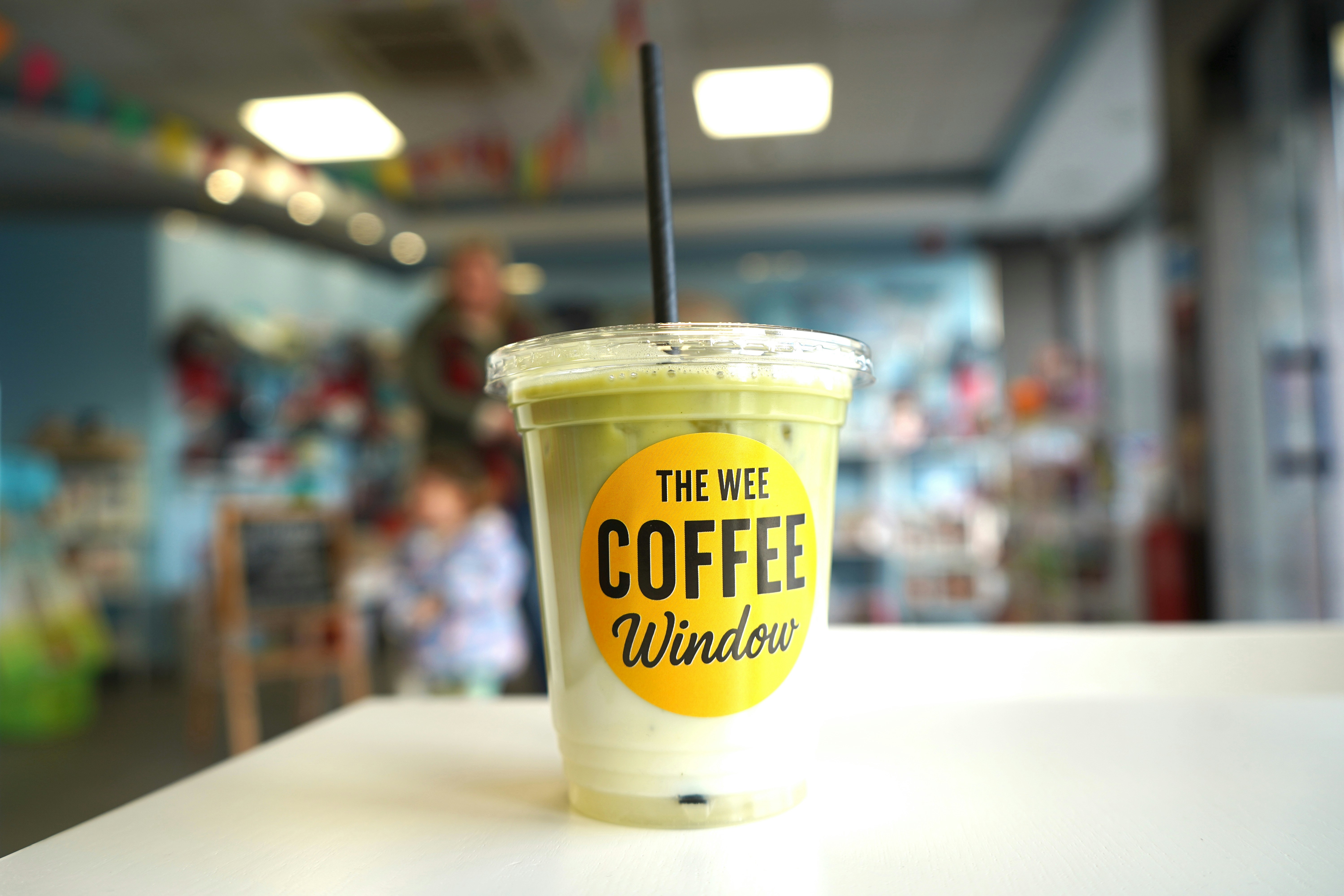 Iced matcha latte with yellow "the wee coffee window" logo.