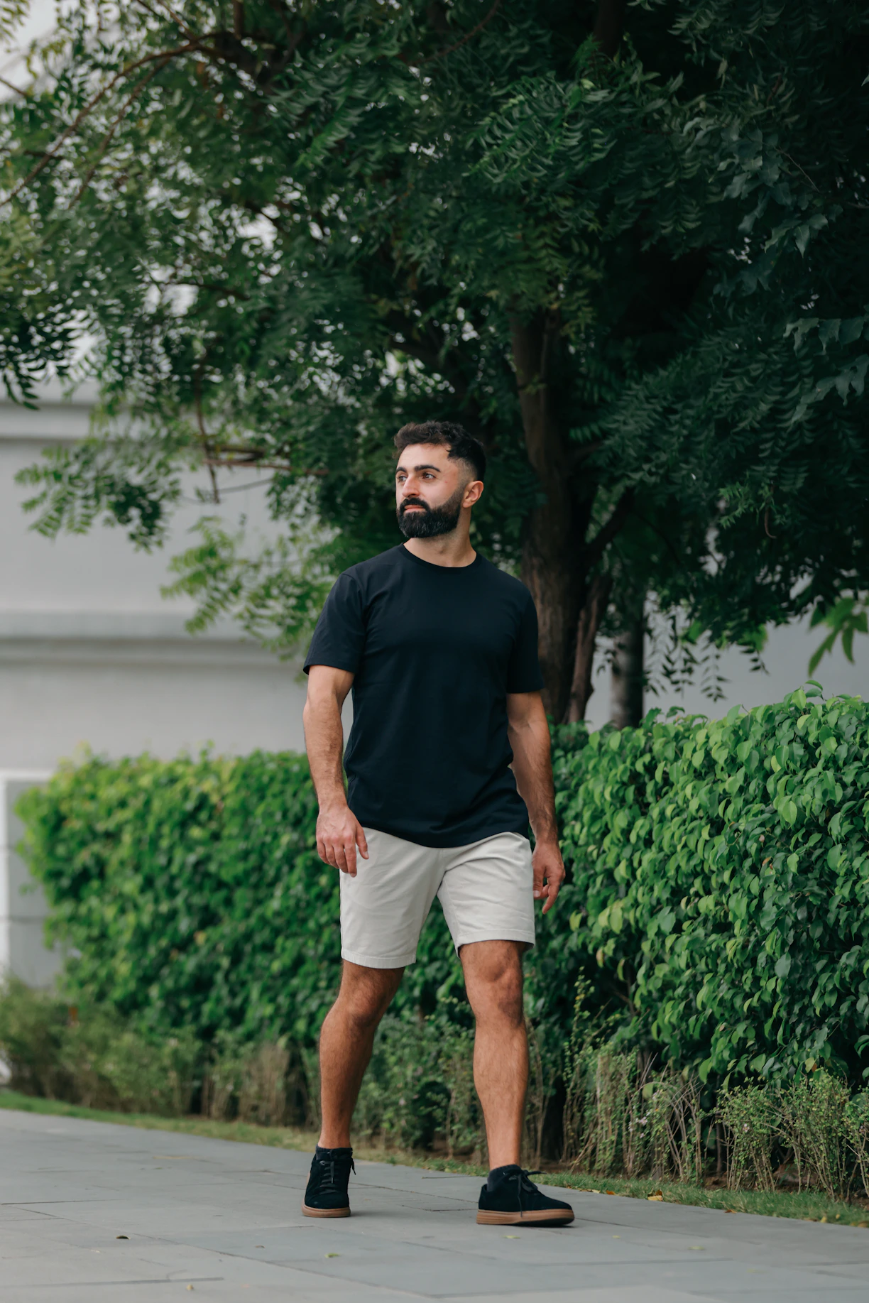 Man with beard walking outdoors near green bushes