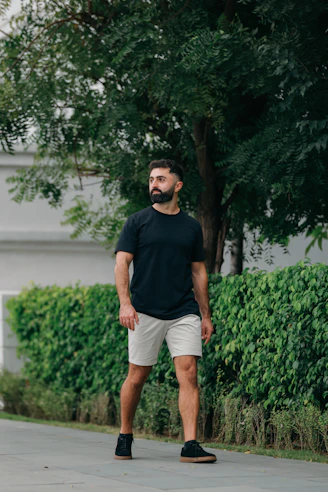 Man with beard walking outdoors near green bushes