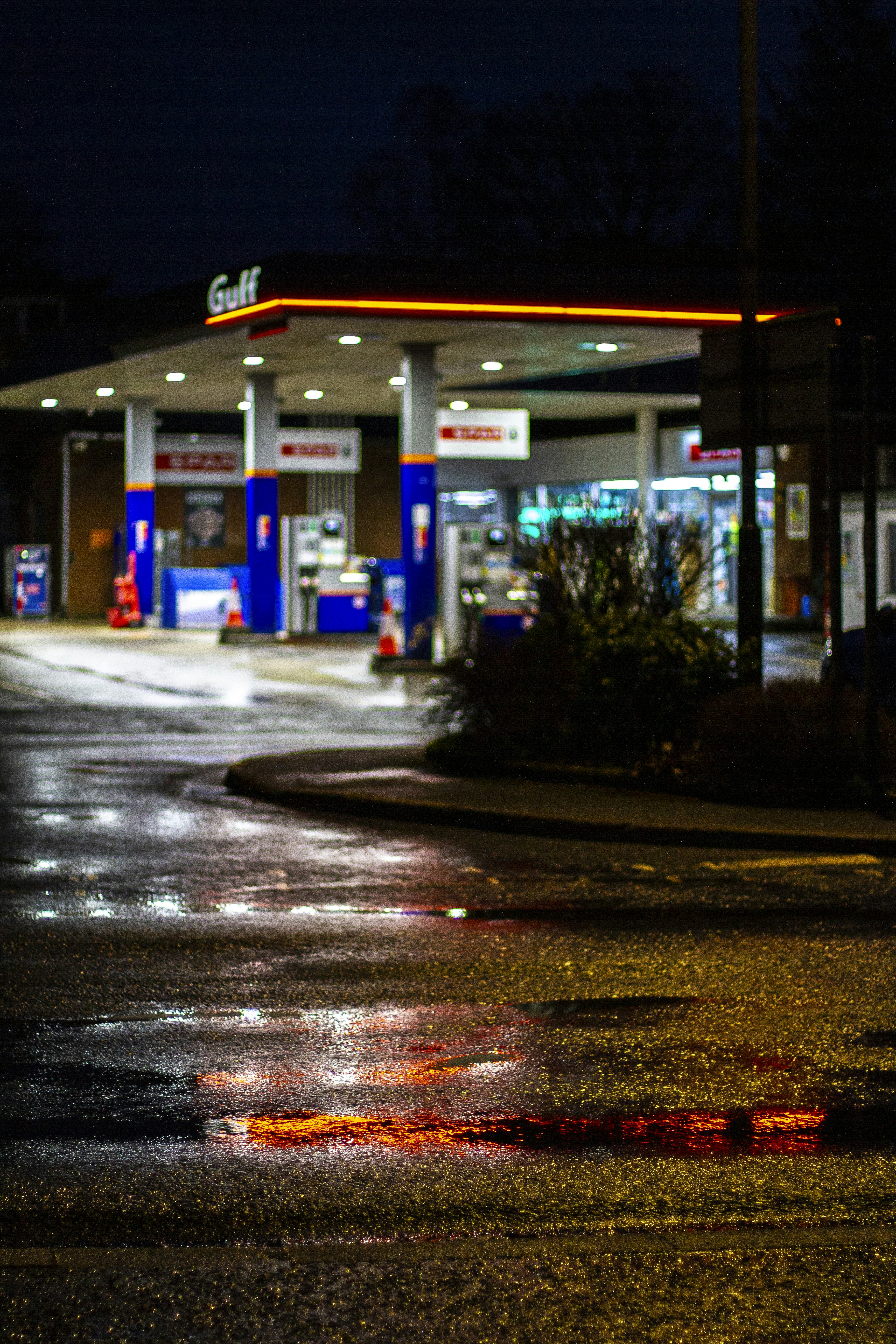 Gasolinera por la noche con el pavimento mojado reflejando las luces