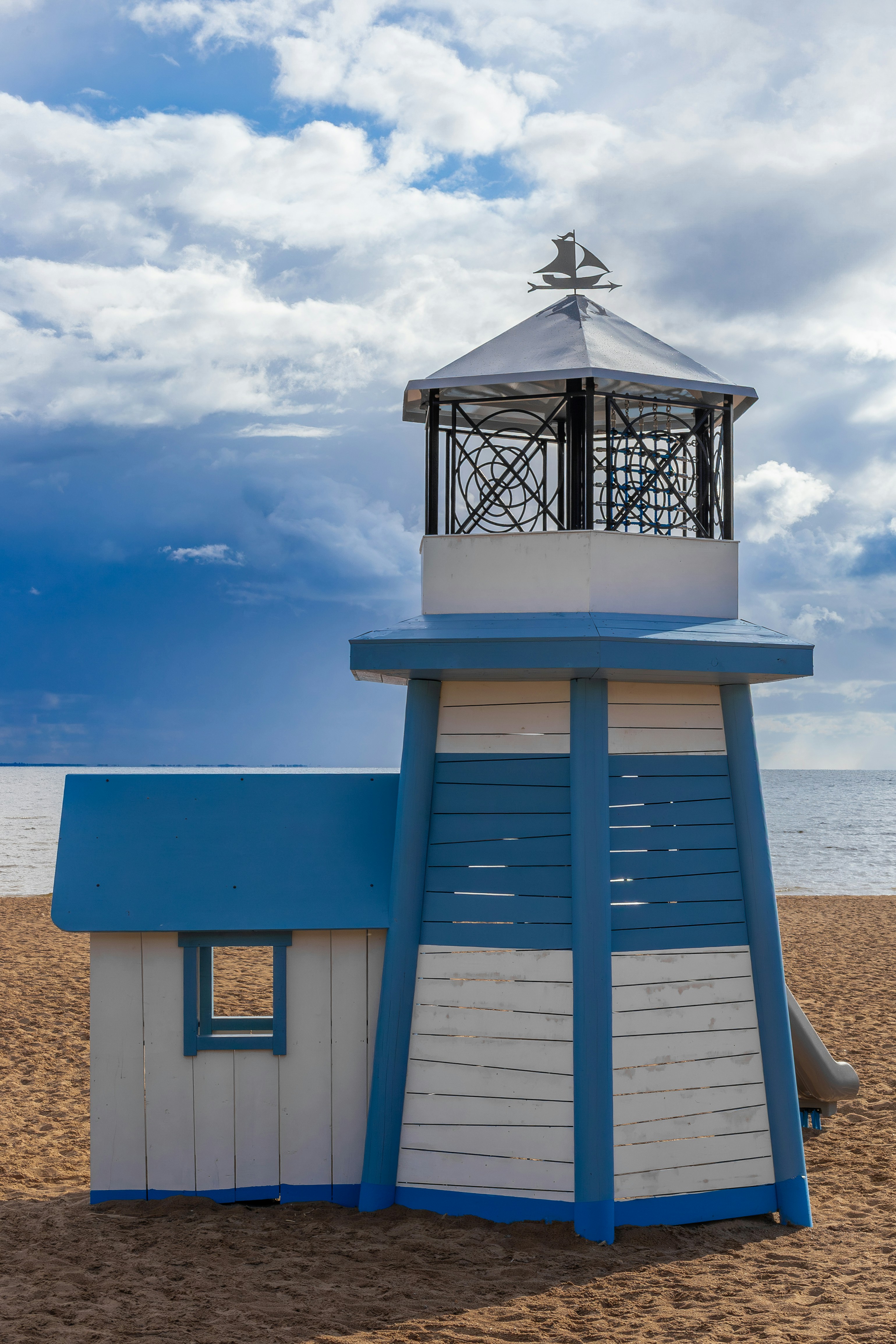 A blue and white lighthouse structure on a sandy beach.