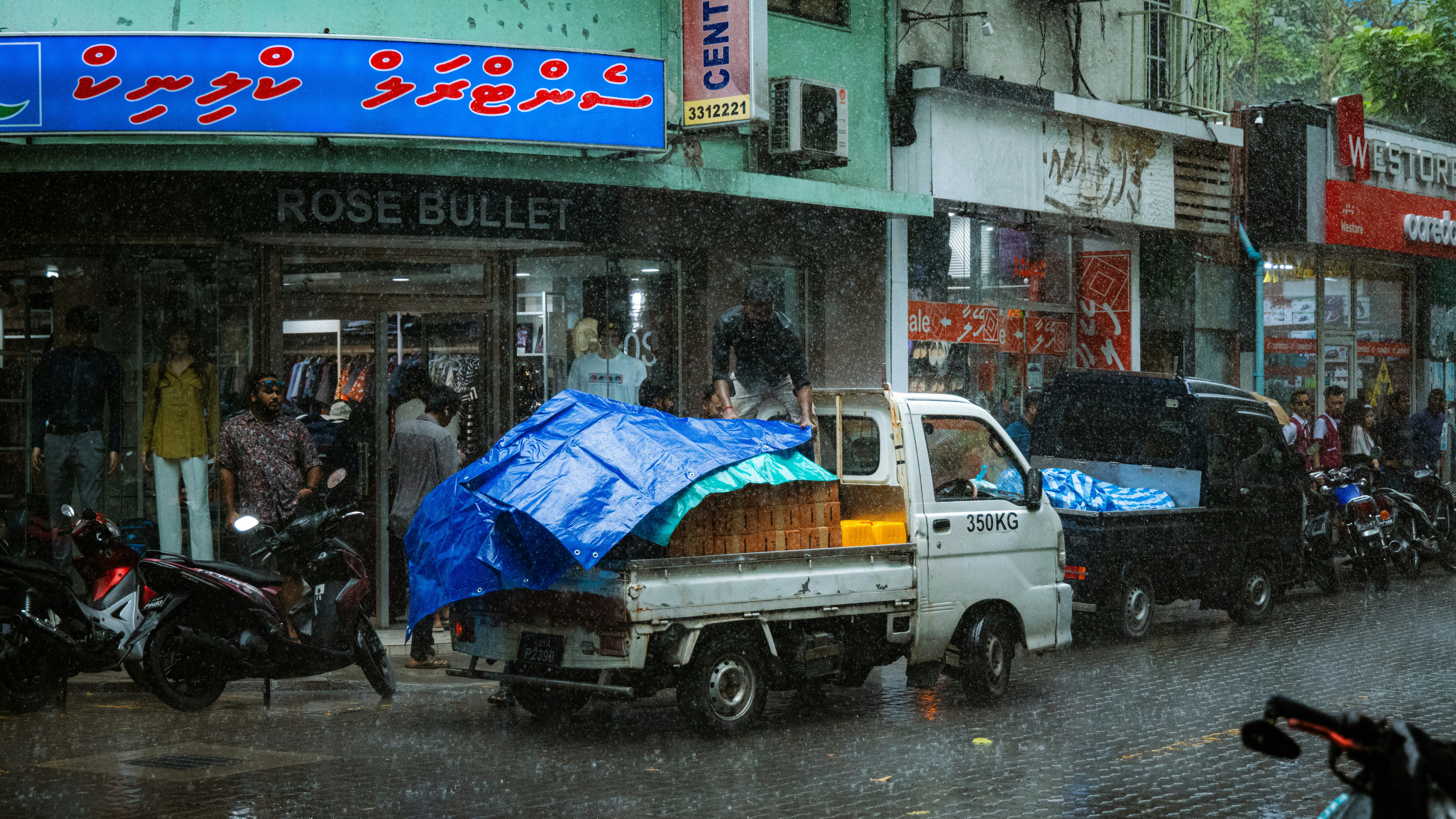 Small truck carrying covered goods in rainy street.