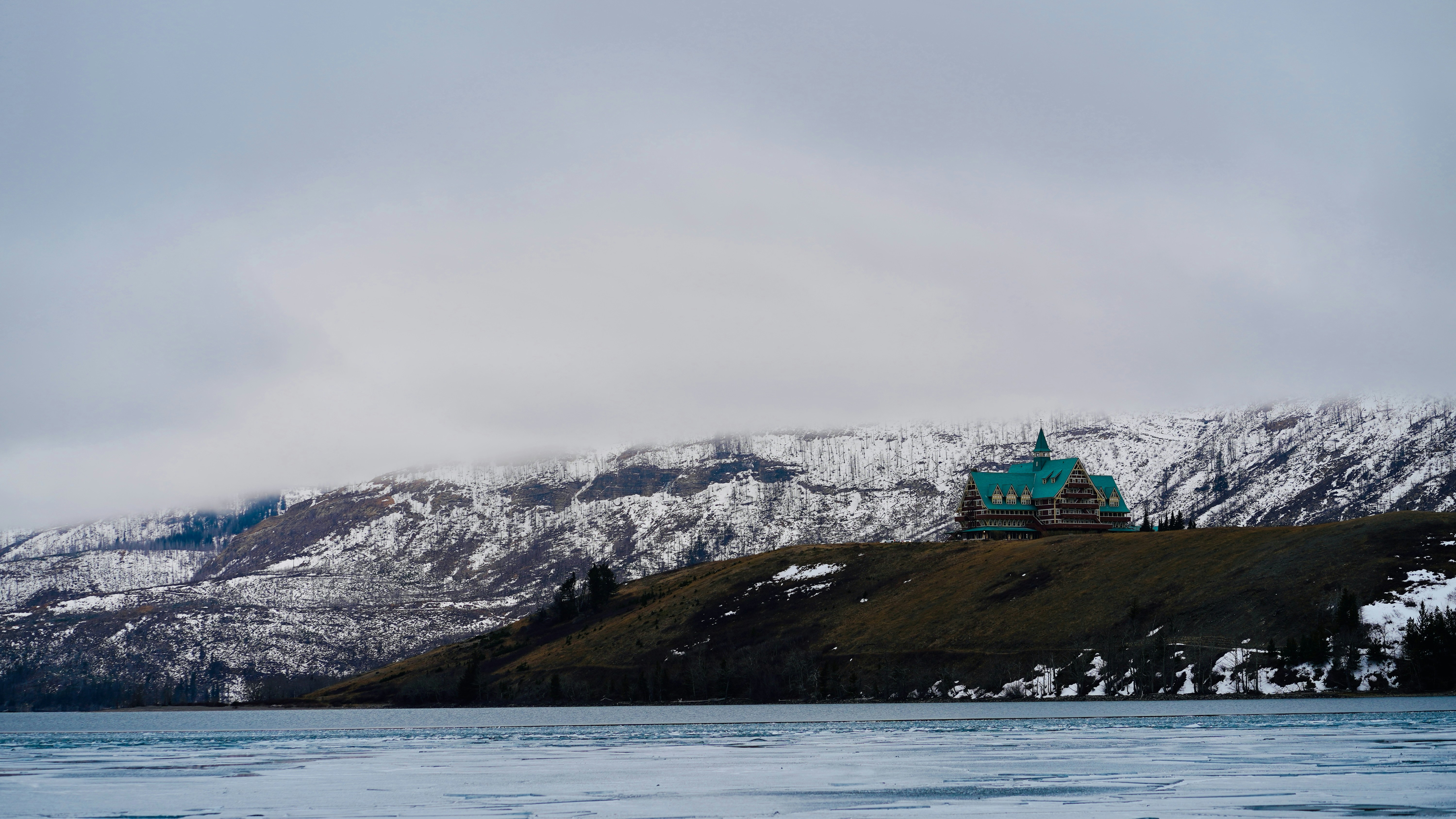 Ein historisches Hotel liegt auf einem verschneiten Hügel mit Blick auf das Wasser.
