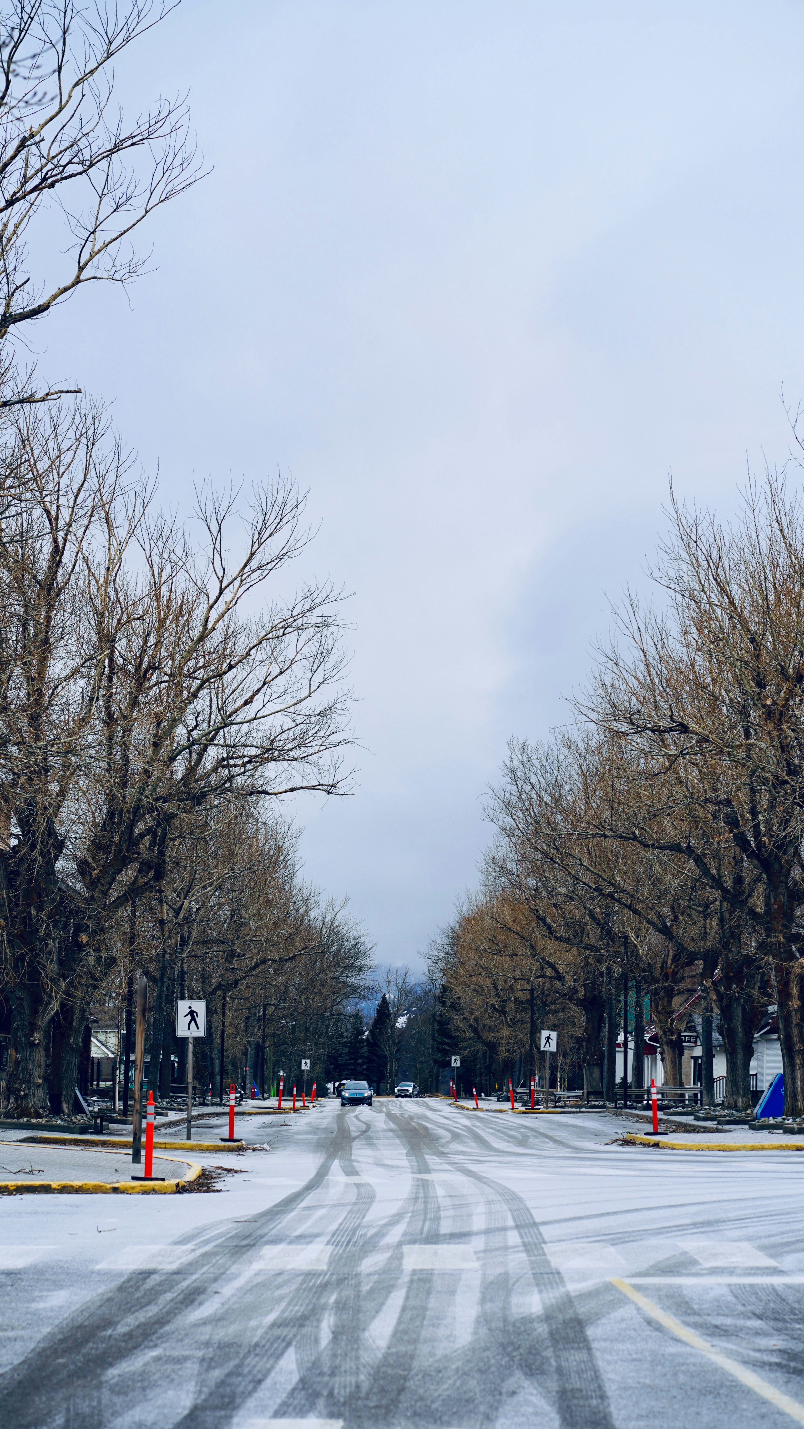 Schneebedeckte Straße, gesäumt von kahlen Bäumen und Reifenspuren.