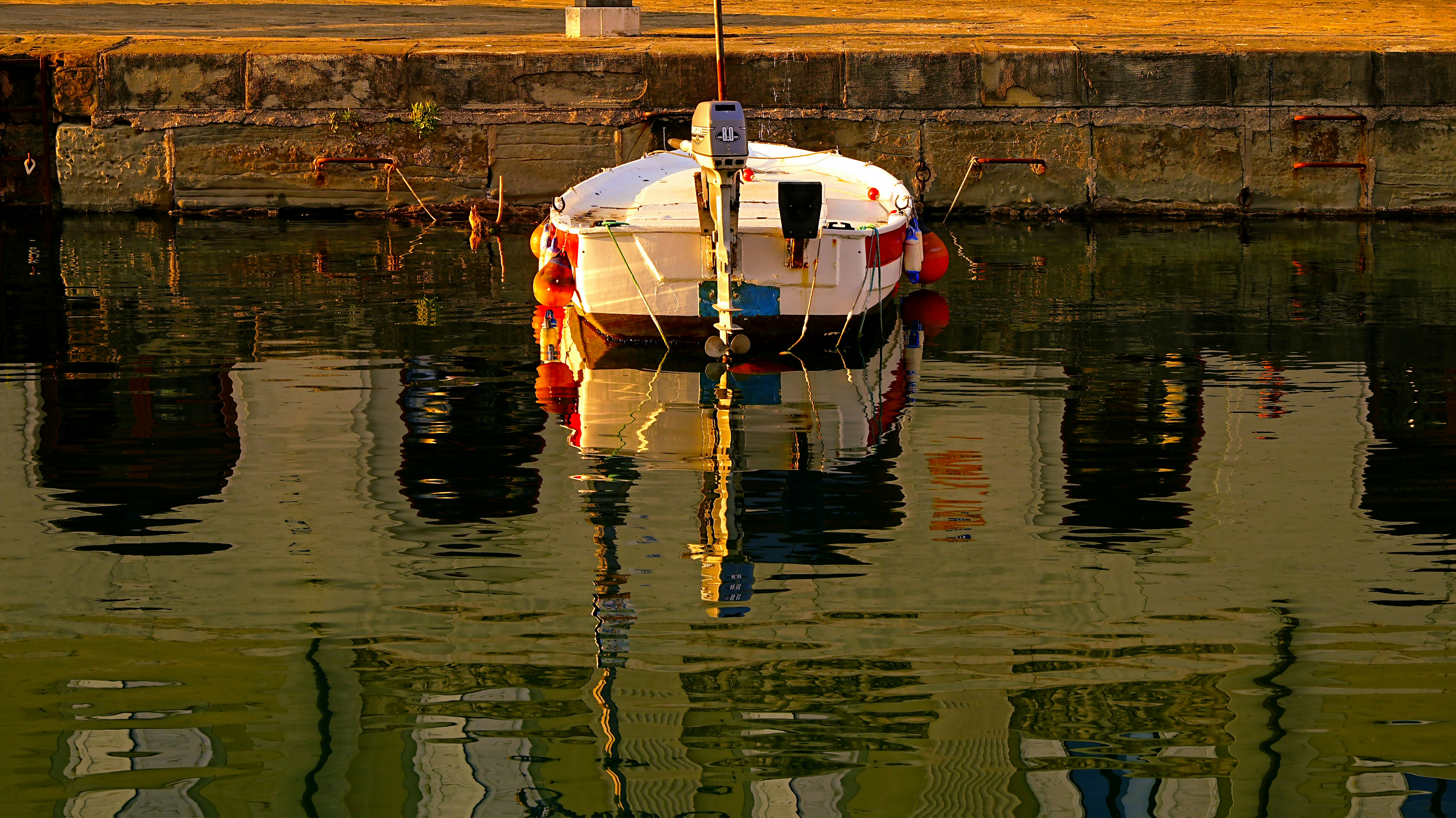 Weißes Boot liegt in ruhigem Wasser mit Spiegelungen.