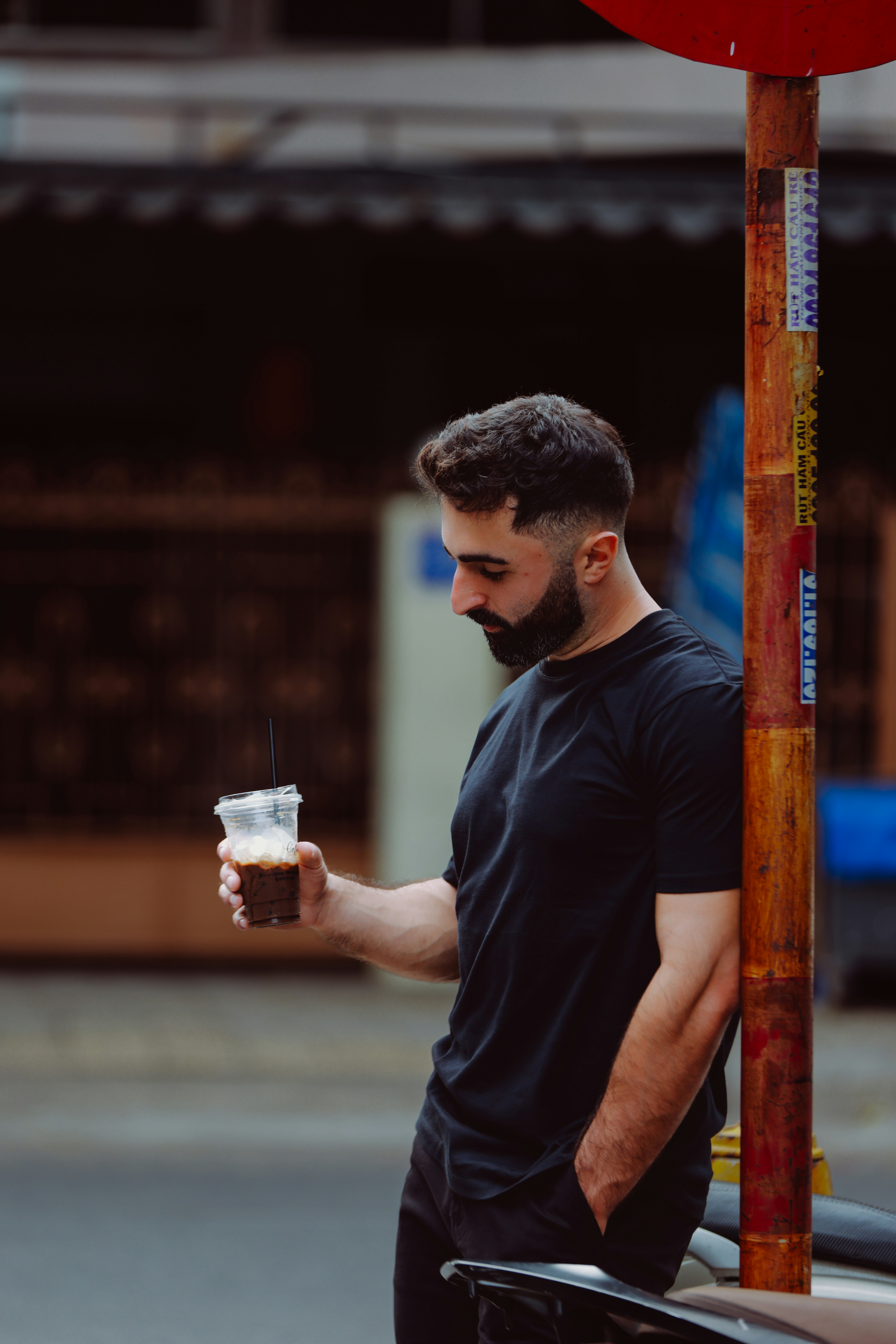 黒いシャツの男性が屋外でコーヒーカップを持っている