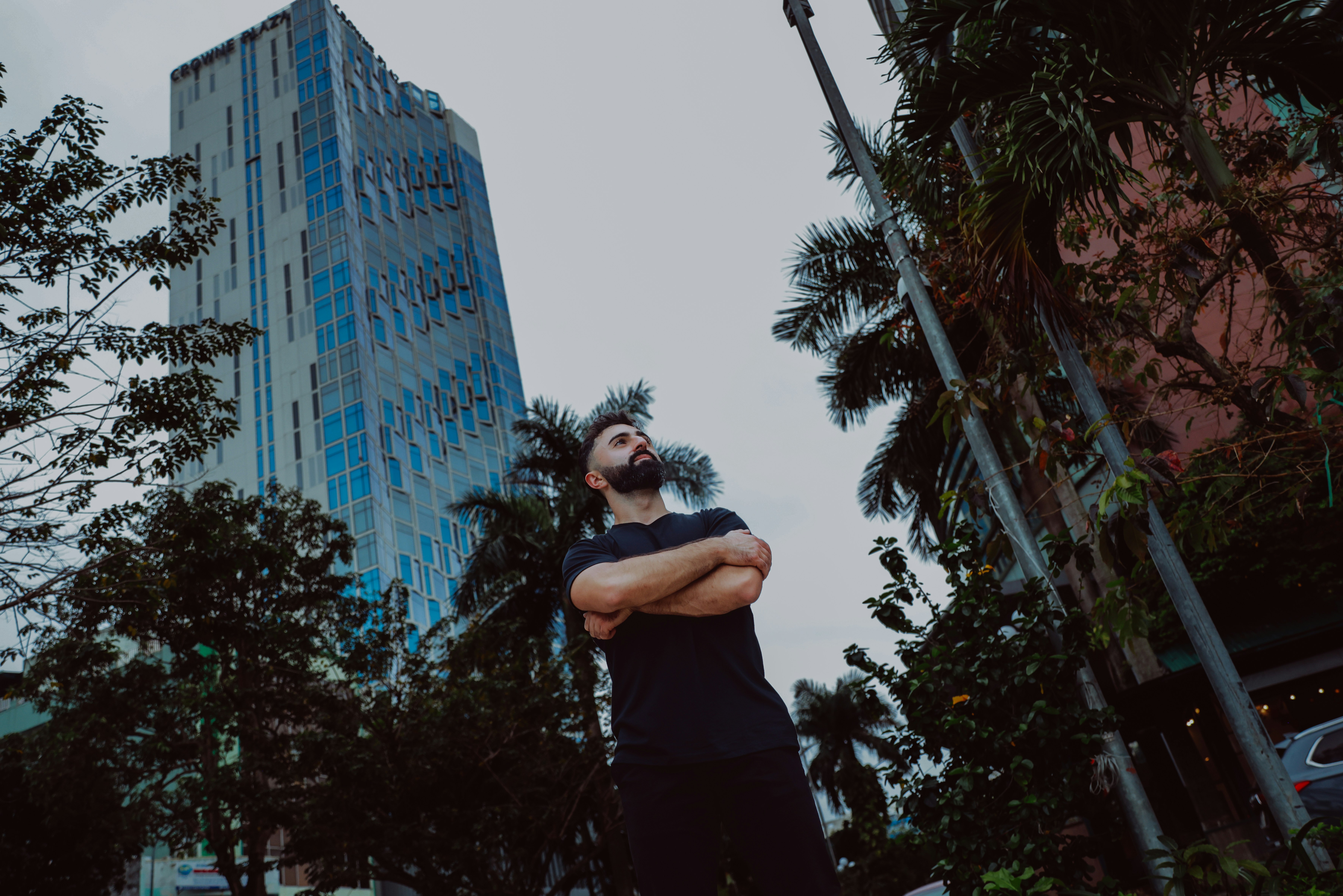 Man with arms crossed looking up at tall building.