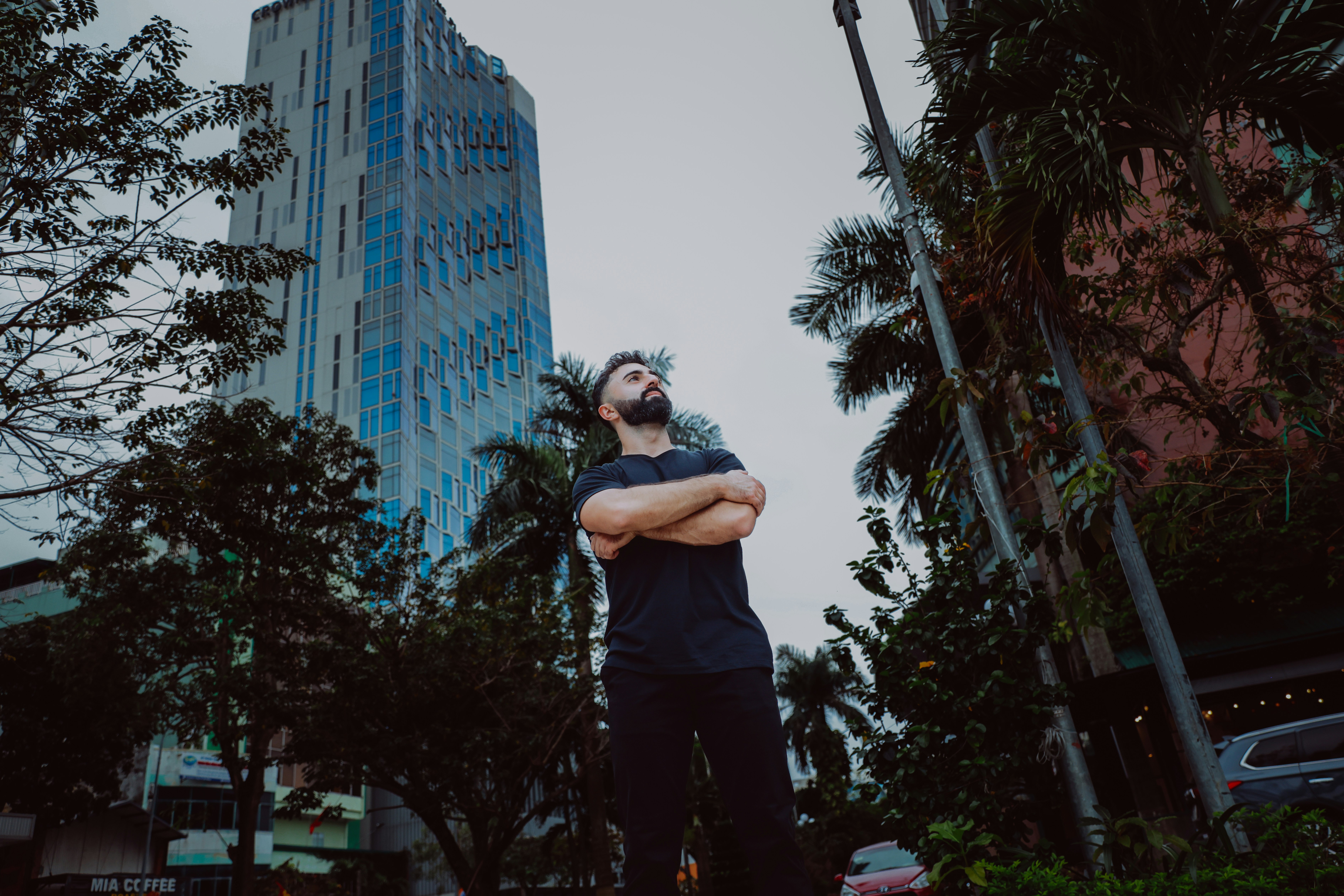 腕を組んだ男が近代的な建物の外に立っている。