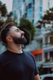 Man with beard looking up at buildings