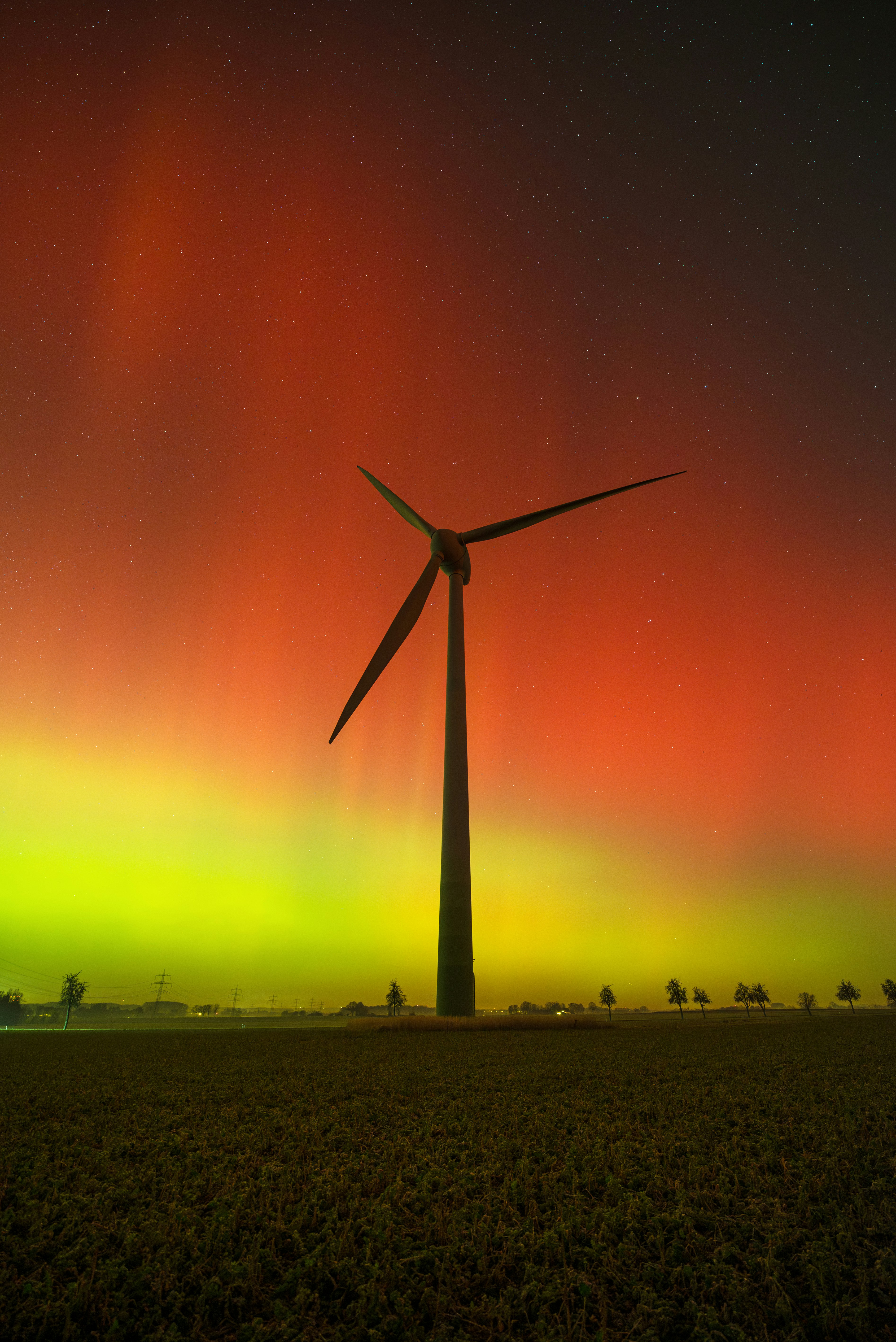 Windturbine silhouetteiert vor dem farbenfrohen Polarlichthimmel