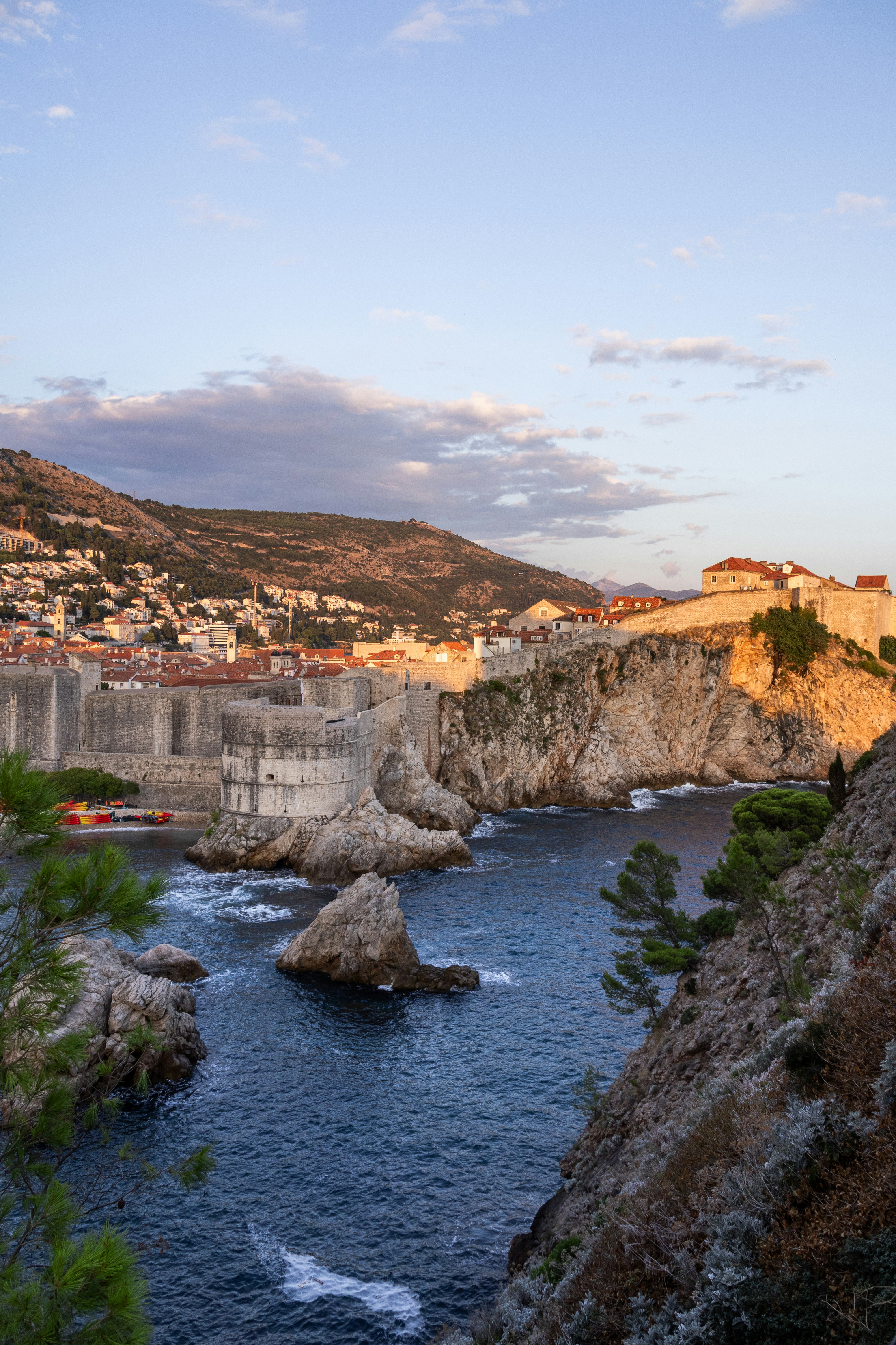 Historic walled city on a rocky coastline at sunset.