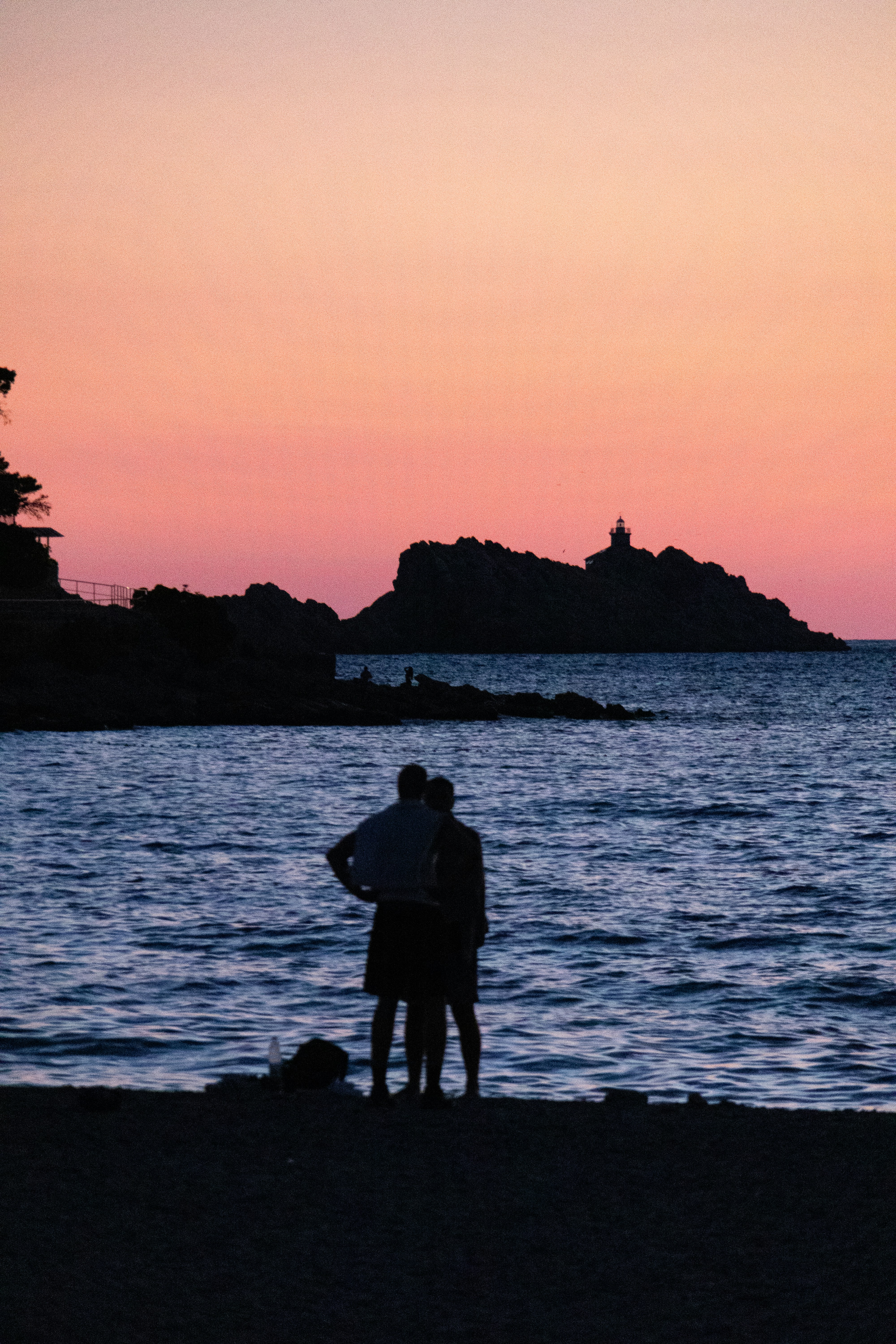 Couple silhouetted on beach watching sunset over ocean.