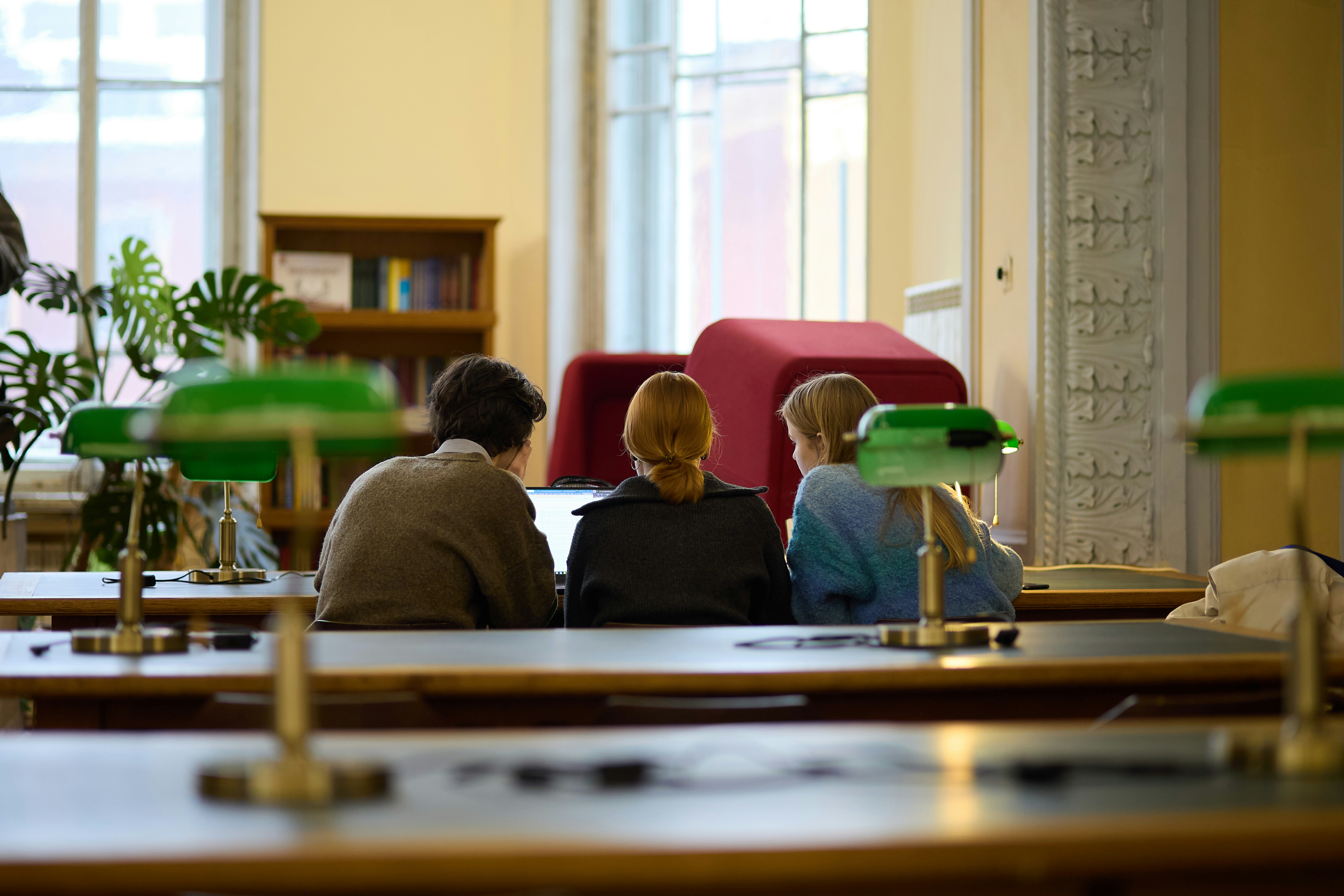 Three people sitting at desks in a library.