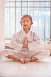 Young girl in white gi meditating with eyes closed.